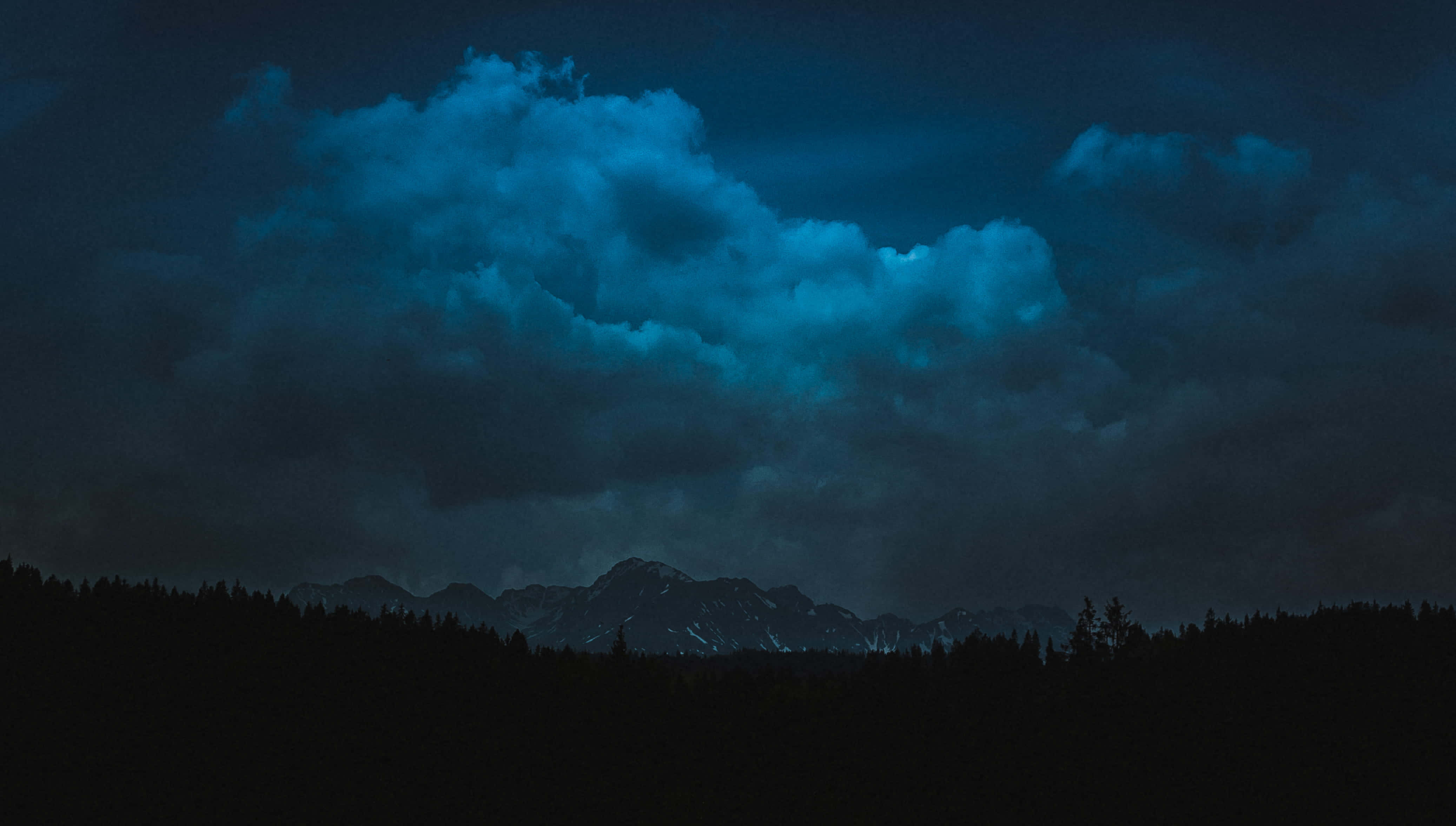 Dark Heaven 桌布 壁紙 — 戲劇性的夜空，發光的藍色雲層籠罩著黑暗的森林和遠處的雪山。