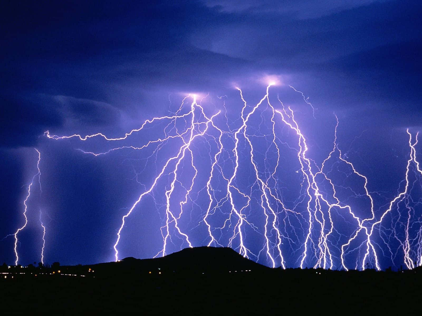 閃電 桌布 壁紙 — 戲劇性的夜空爆發多道鮮豔紫色閃電，擊落在黑暗剪影的山丘上。