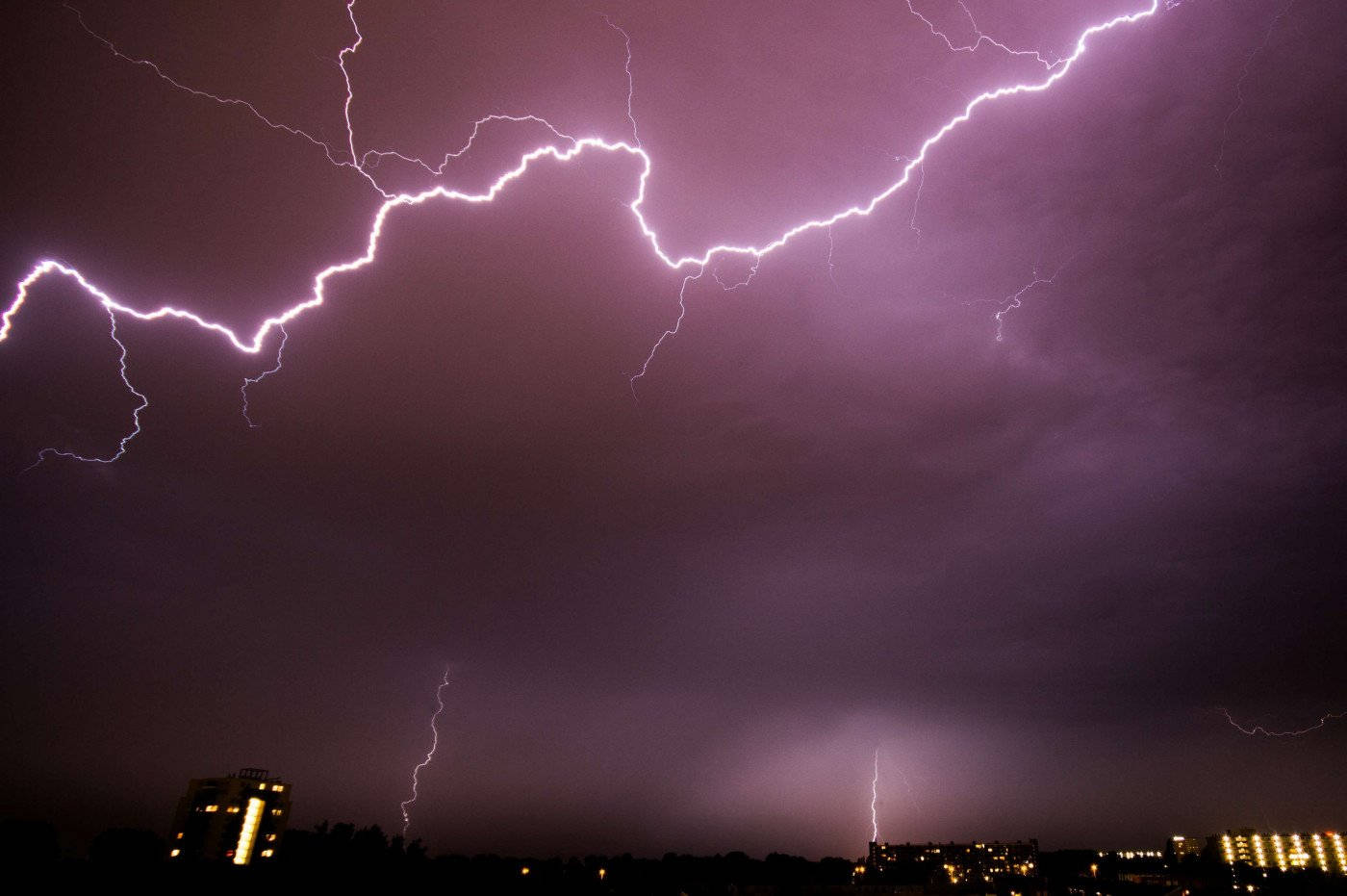 Thunderstorm 桌布 壁紙 — 戲劇性的夜空被鮮豔的紫色閃電照亮，城市天際線中建築物閃爍著光芒。
