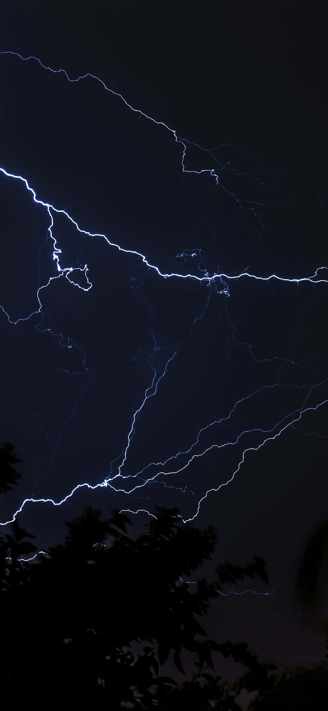 Lightning Bolt iPhone 桌布 壁紙 — 戲劇性的夜空被鮮豔的藍色閃電劈開，照亮了黑暗的雲層和下方的樹木剪影。