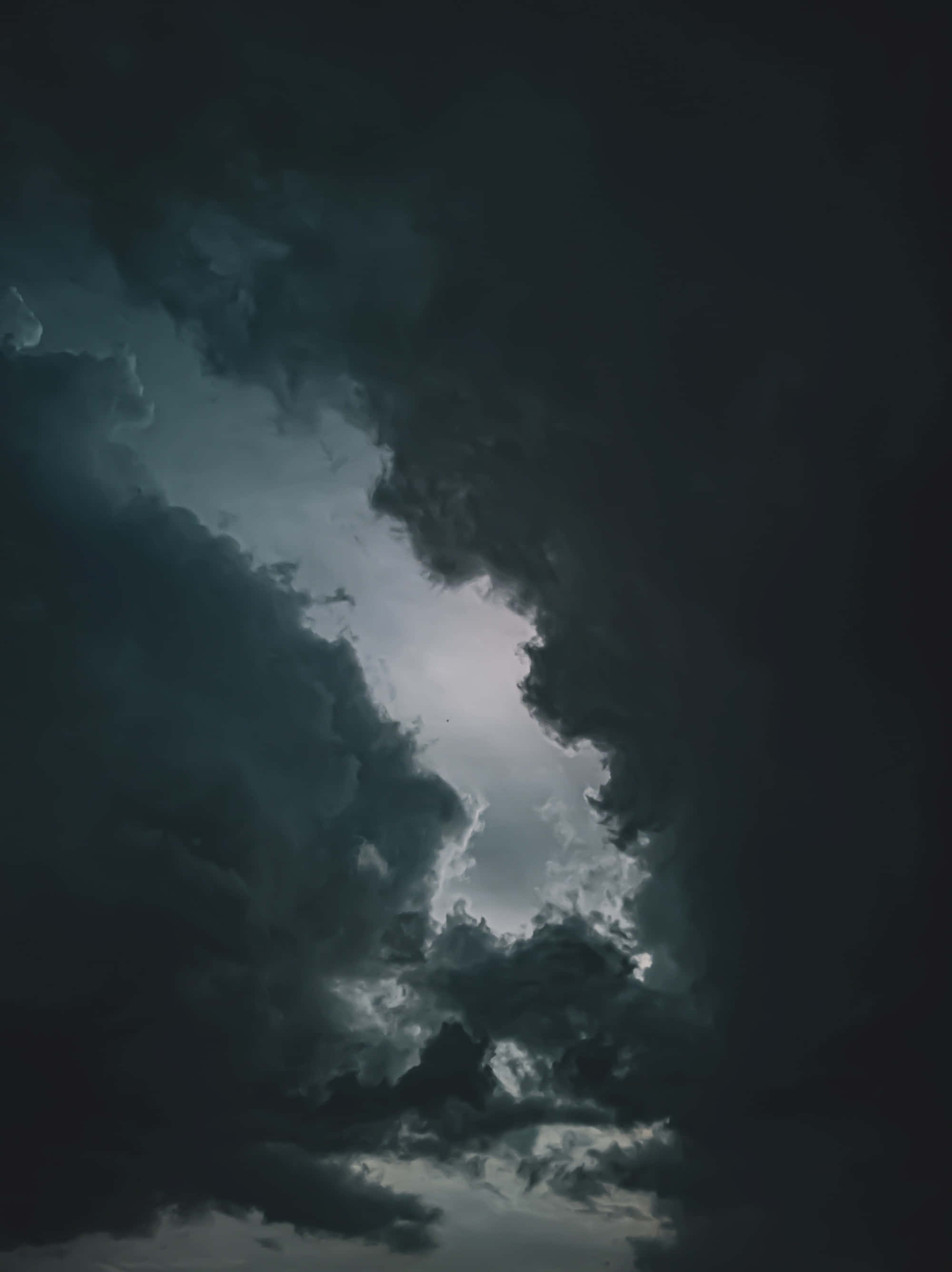夜空 桌布 壁紙 — 戲劇性的天空，烏黑的風暴雲層分開，露出上方明亮的發光開口。