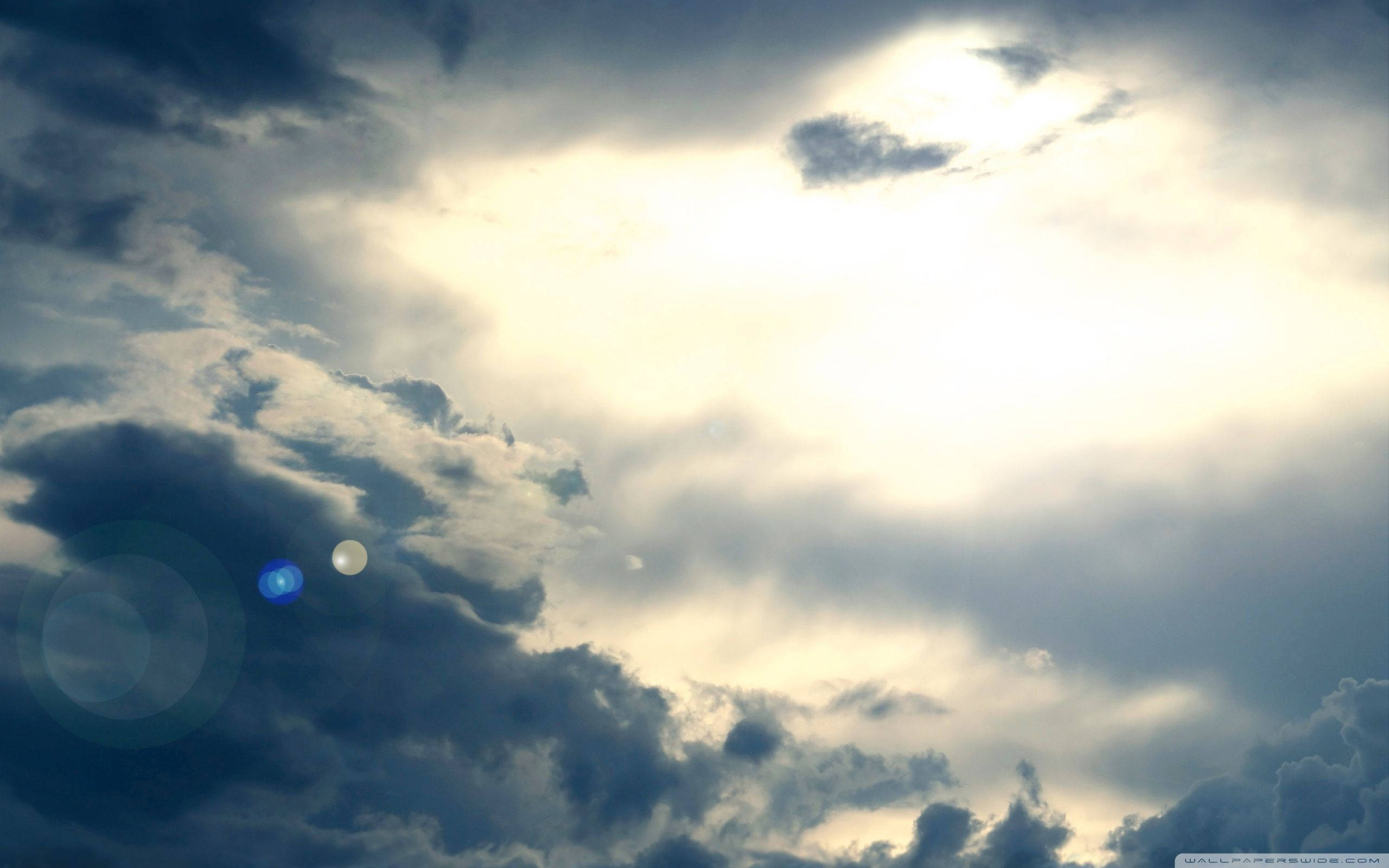 Heavenly Clouds 桌布 壁紙 — 戲劇性的天空，陽光穿透烏雲，投射出金色光芒和鏡頭光暈。