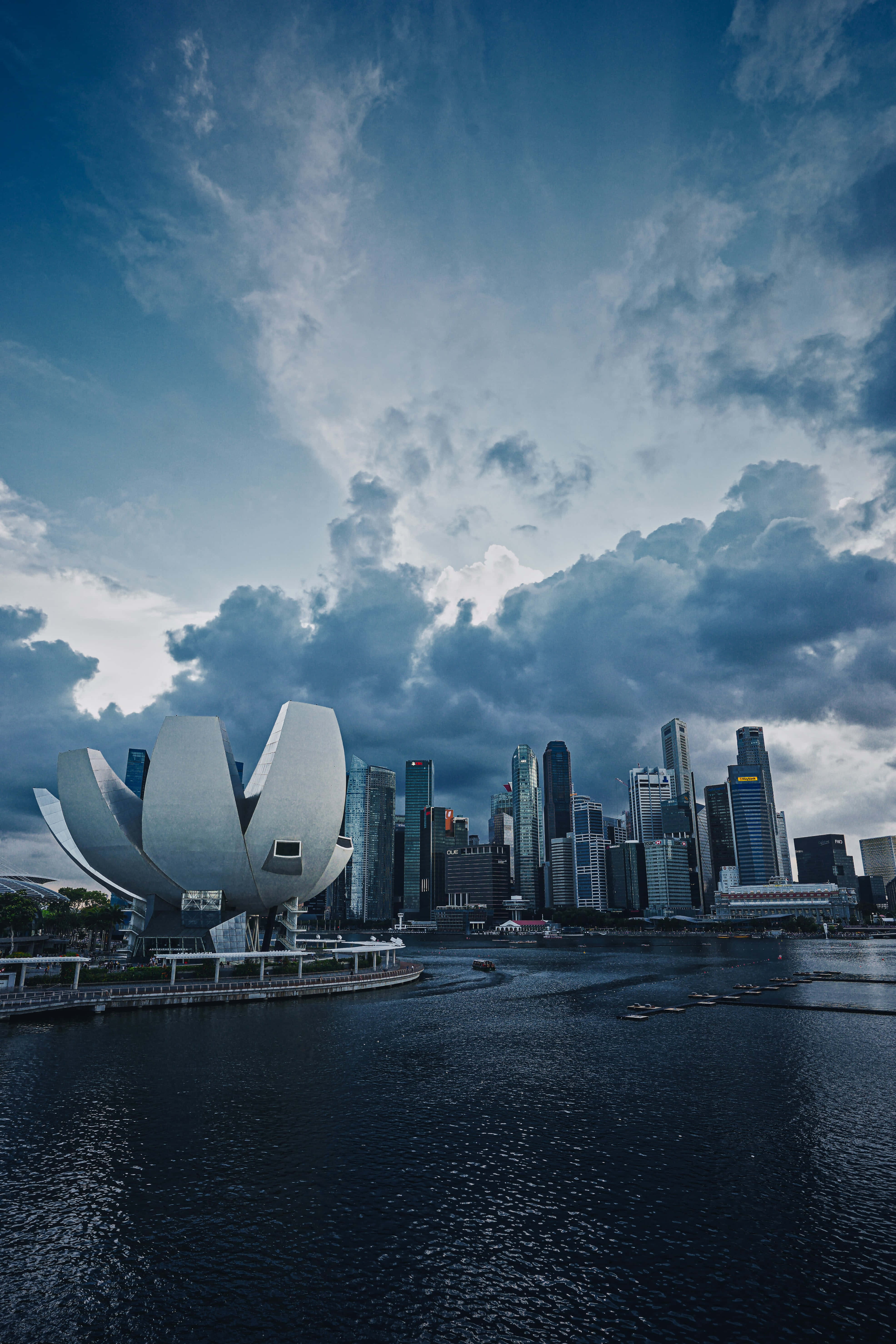 Singapore 桌布 壁紙 — 戲劇性的天空烏雲密佈，籠罩著新加坡標誌性的藝術科學博物館，現代天際線倒映在平靜的水面上。