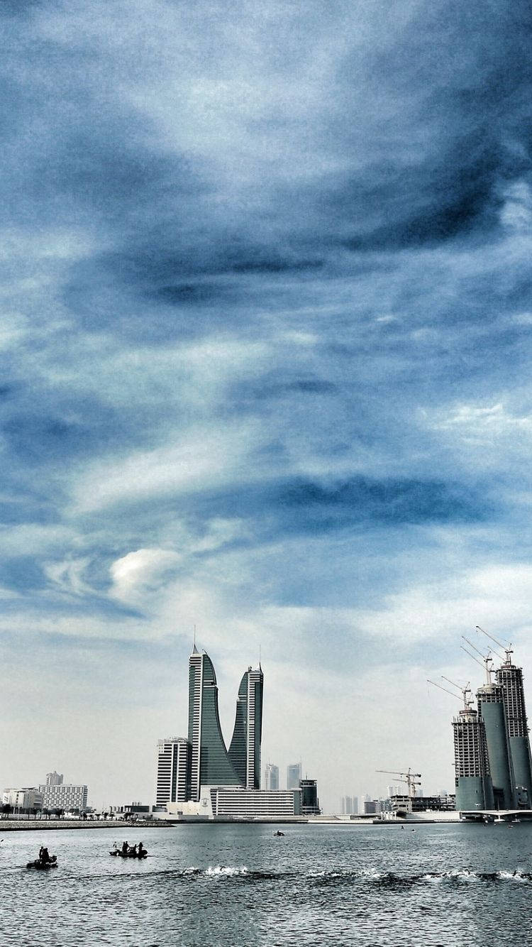 Bahrain 桌布 壁紙 — 戲劇性的天空籠罩著現代摩天大樓和建築起重機，旁邊是停有小船的水道。