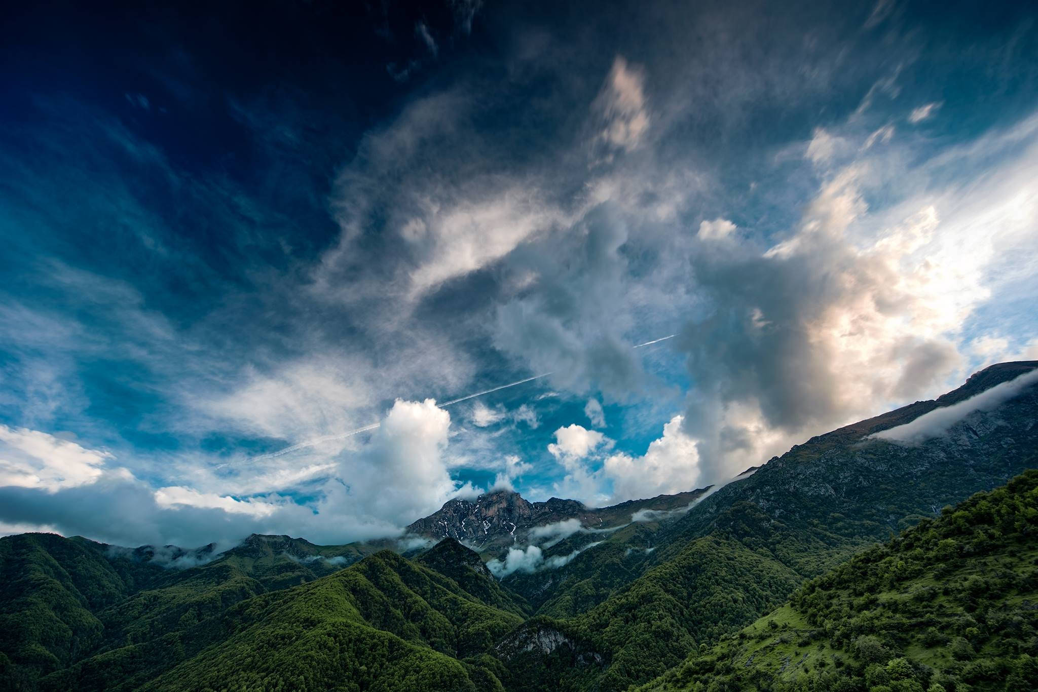 Armenia 桌布 壁紙 — 戲劇性的山峰在廣闊的天空下聳立，天空充滿旋轉的雲層，一道明亮的陽光穿透而過。