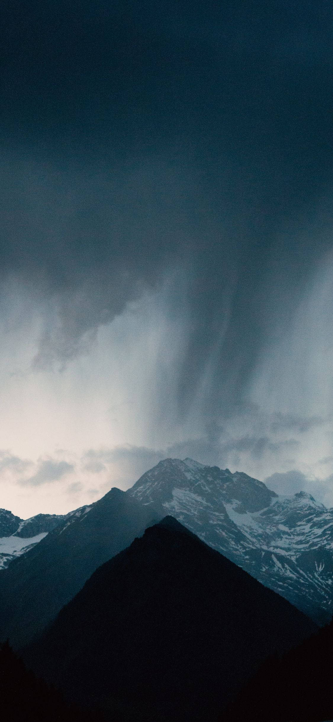 桌布 壁紙 — 戲劇性的山峰在暴風雨的天空下呈現剪影，大雨如厚重的簾幕般傾瀉而下。