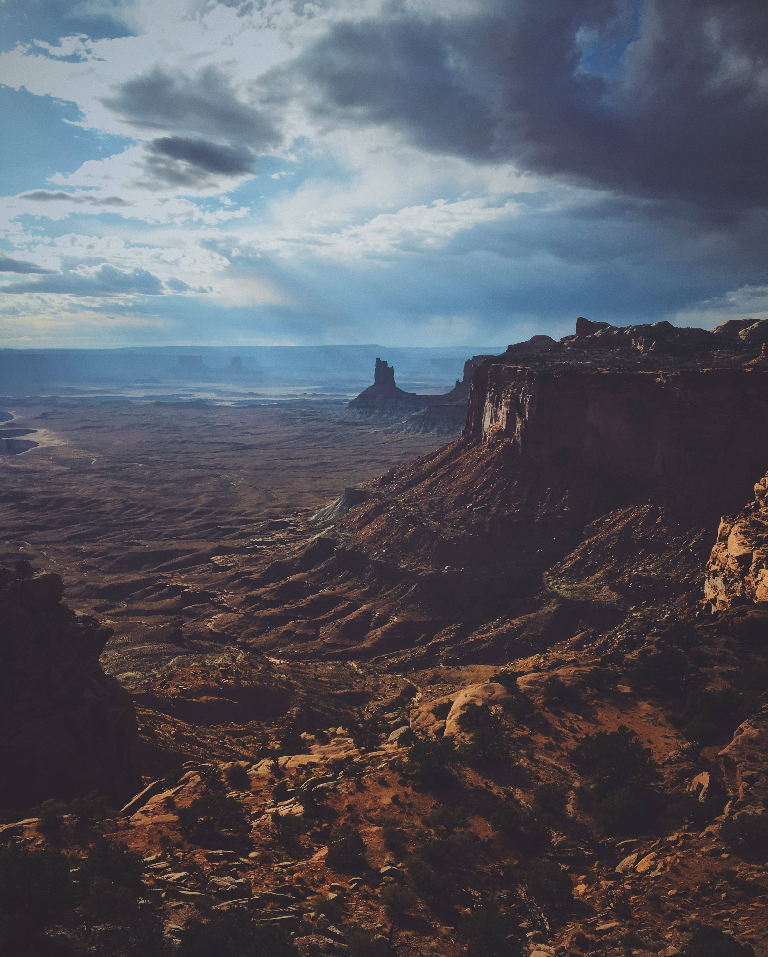 Canyonlands National Park 桌布 壁紙 — 戲劇性的峽谷景觀，高聳的紅色岩層在陰沉天空下，陽光穿透雲層照射下來。