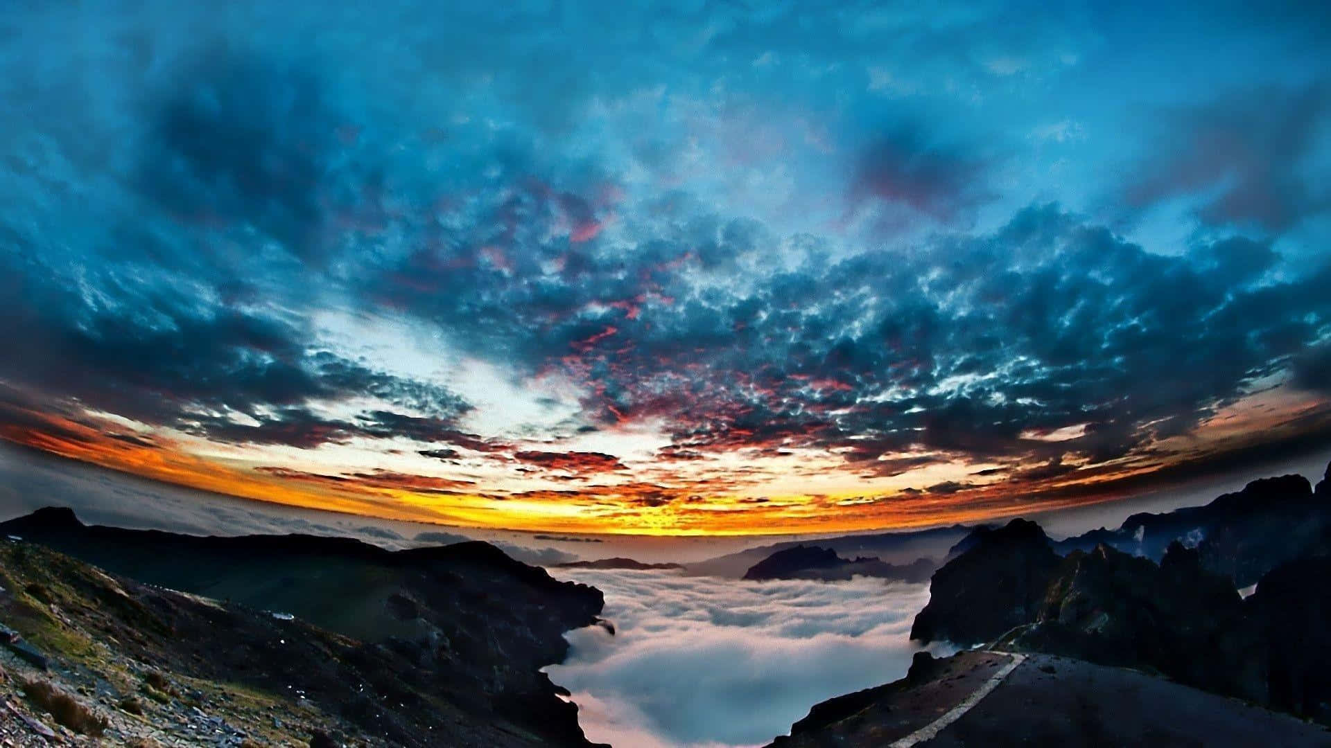 Fisheye 桌布 壁紙 — 戲劇性的日出在崎嶇的山峰之間繪出燃燒的橙色雲彩，下方是霧海。