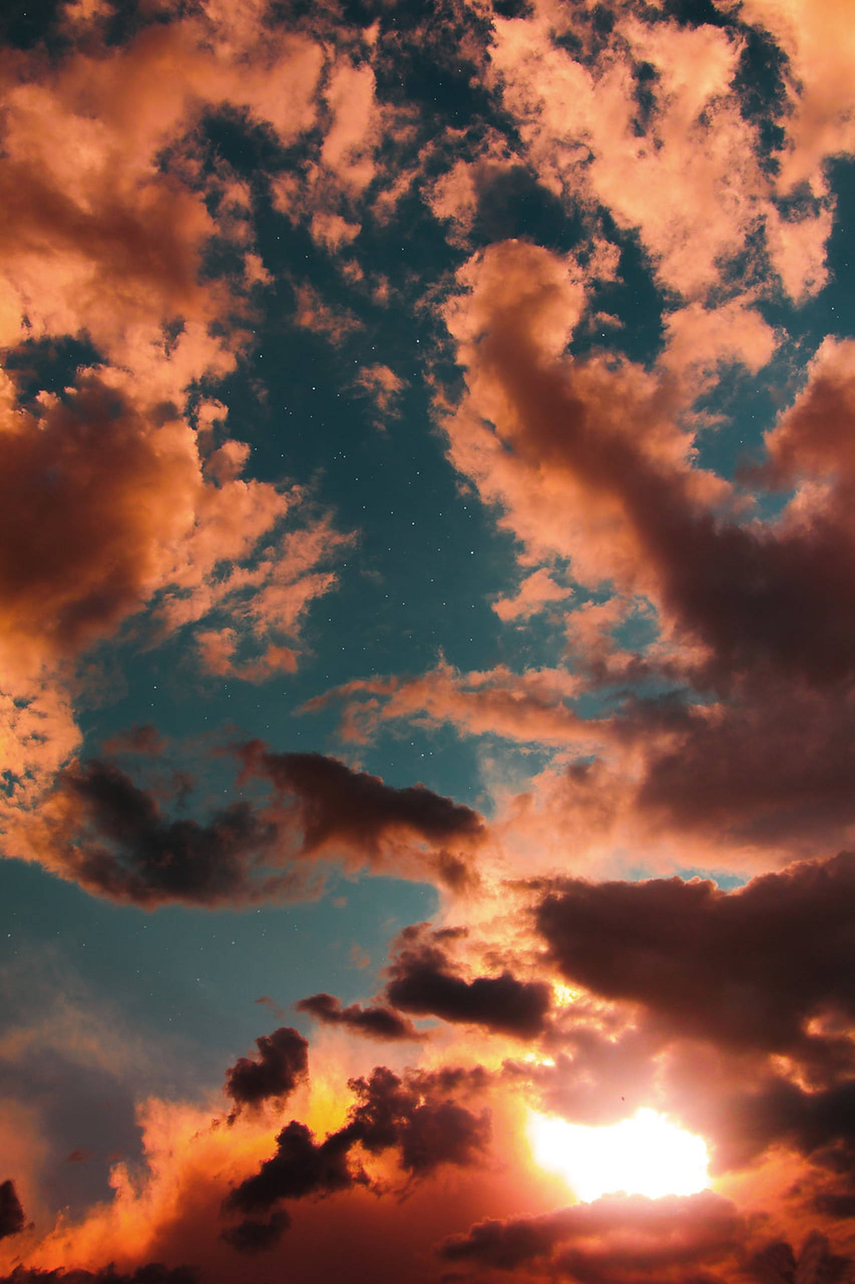 夕陽天空 桌布 壁紙 — 戲劇性的日落，火橙色的雲彩在深藍綠色的天空中閃耀，天空點綴著星星。