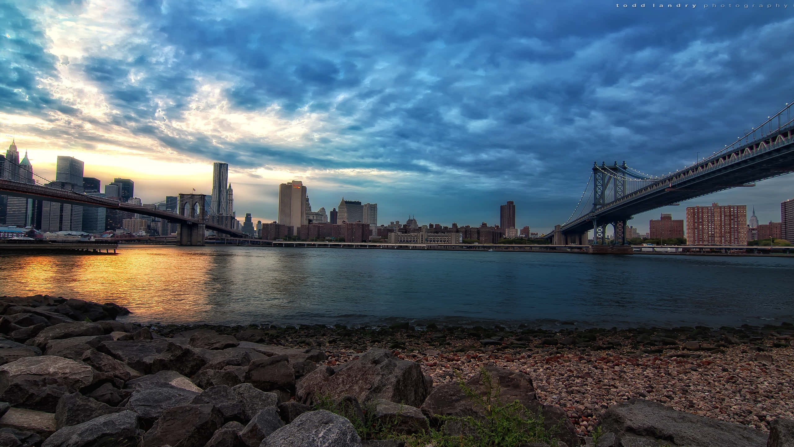 New York City Landscape 桌布 壁紙 — 戲劇性的日落，紐約市天際線，布魯克林大橋和曼哈頓大橋在金色雲彩和漣漪水面上形成剪影。