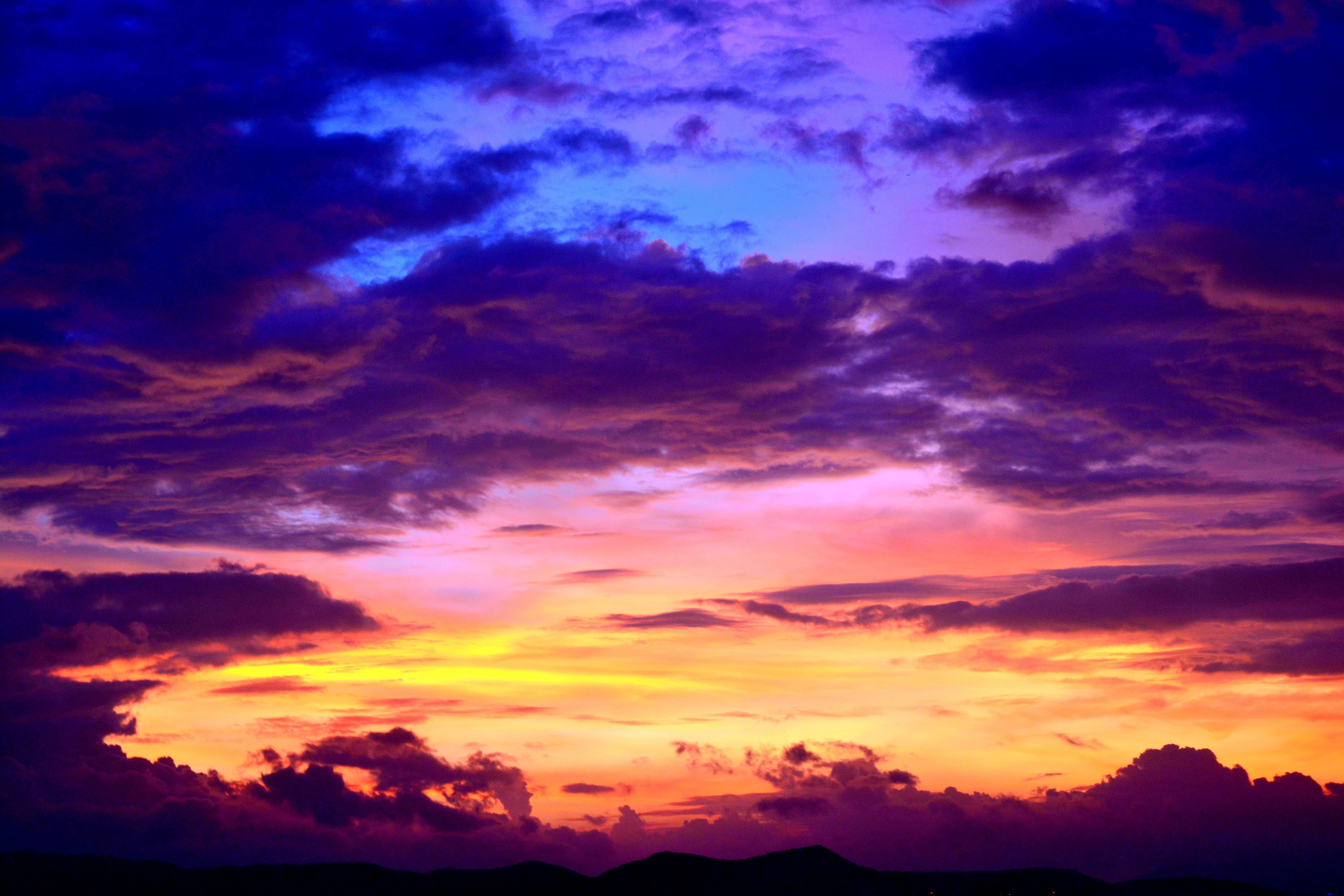Aesthetic Sky 桌布 壁紙 — 戲劇性的日落天空，以火橙色、黃色和深紫色雲彩繪製，映襯著黑暗的山巒輪廓。