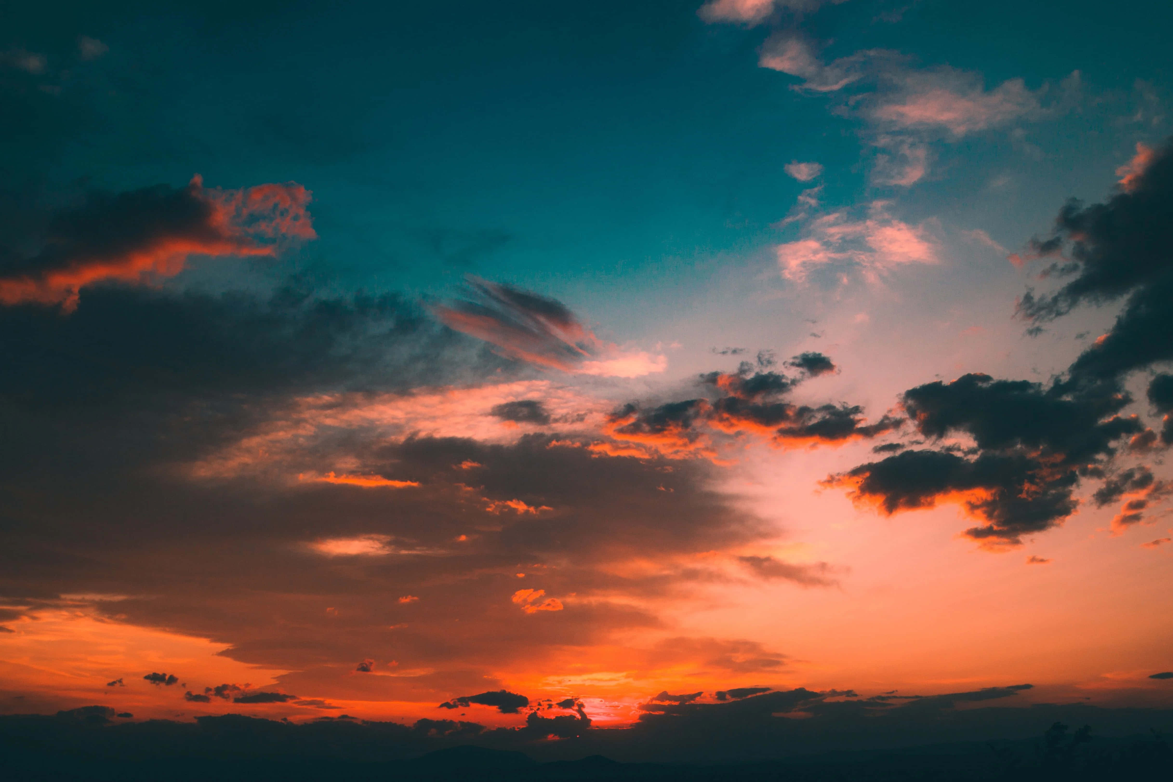 Colorful Sky 桌布 壁紙 — 戲劇性的日落天空，火橙色的雲彩映襯著深藍綠色的地平線。