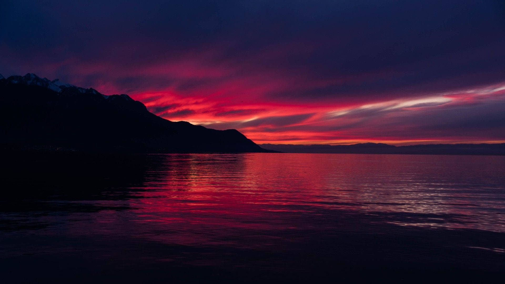 Ocean Sunset 桌布 壁紙 — 戲劇性的日落將天空和水面染成火紅和深紫色，映襯著山巒的剪影。