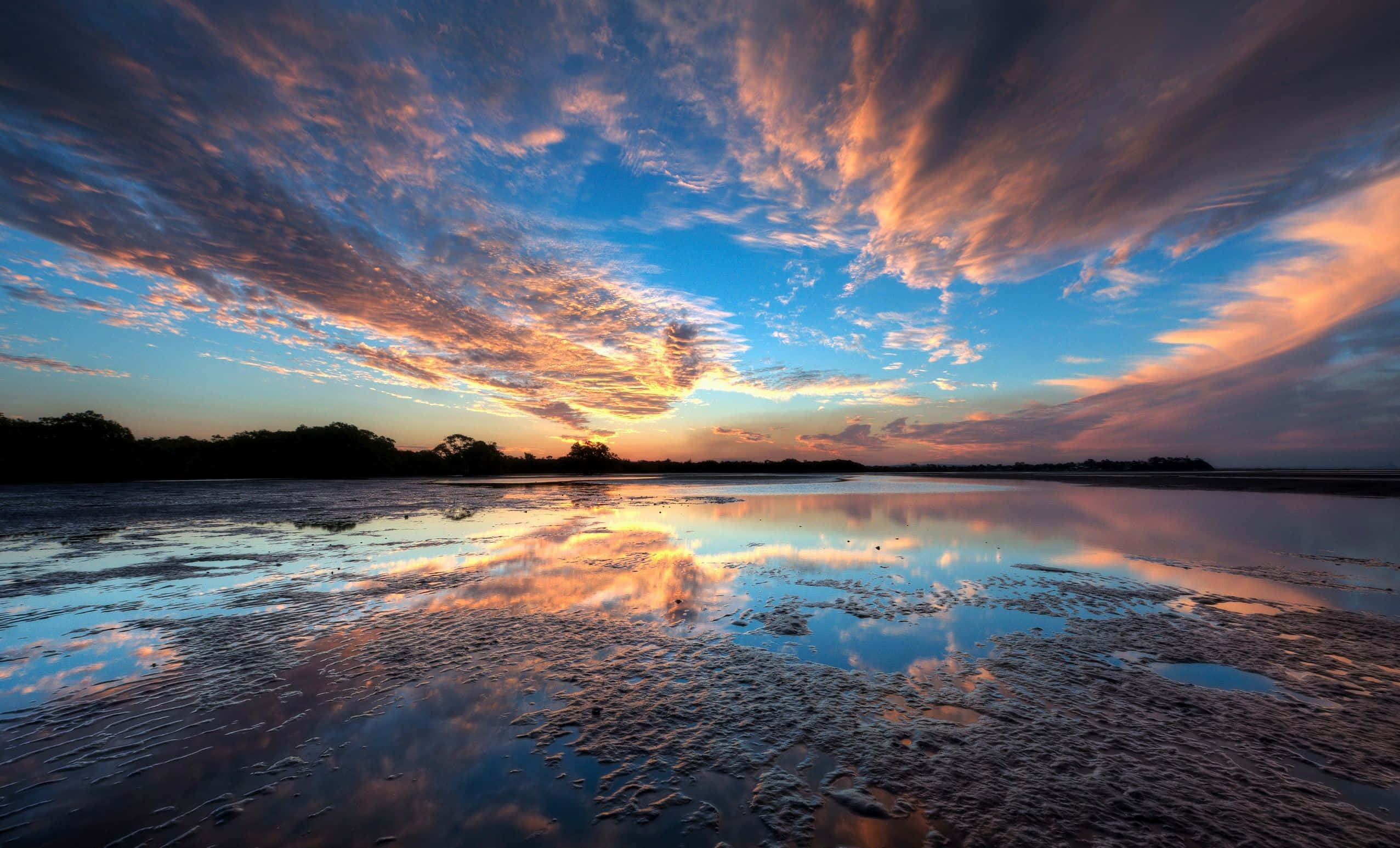 Beautiful Sky 桌布 壁紙 — 戲劇性的日落將天空染成火熱的橙色和深藍色，完美地映照在平靜、有紋理的濕地上。
