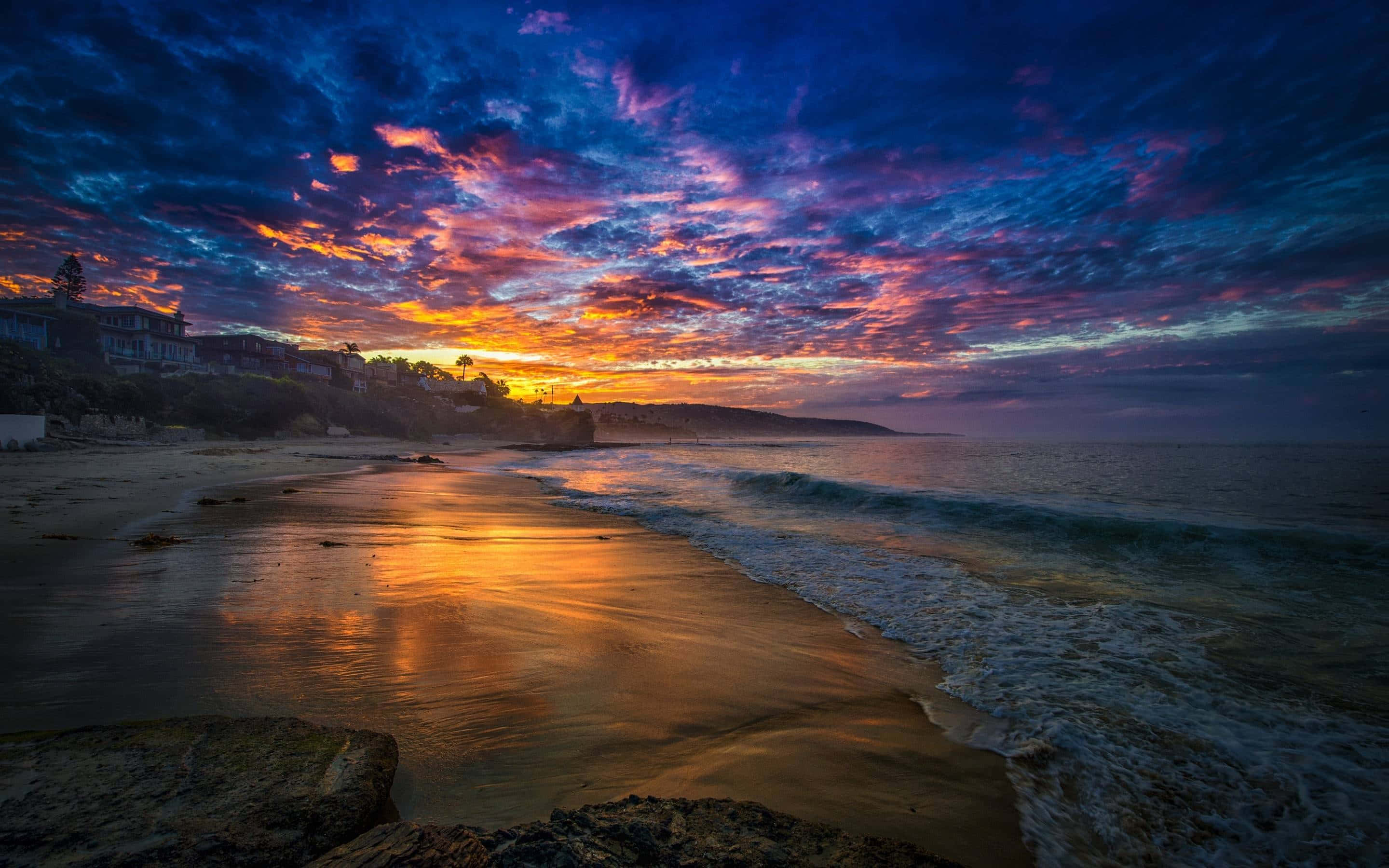 Beautiful Beach 桌布 壁紙 — 戲劇性的日落用火熱的橙色和深紫色描繪天空，下方是平靜的海灘和溫柔的海浪。