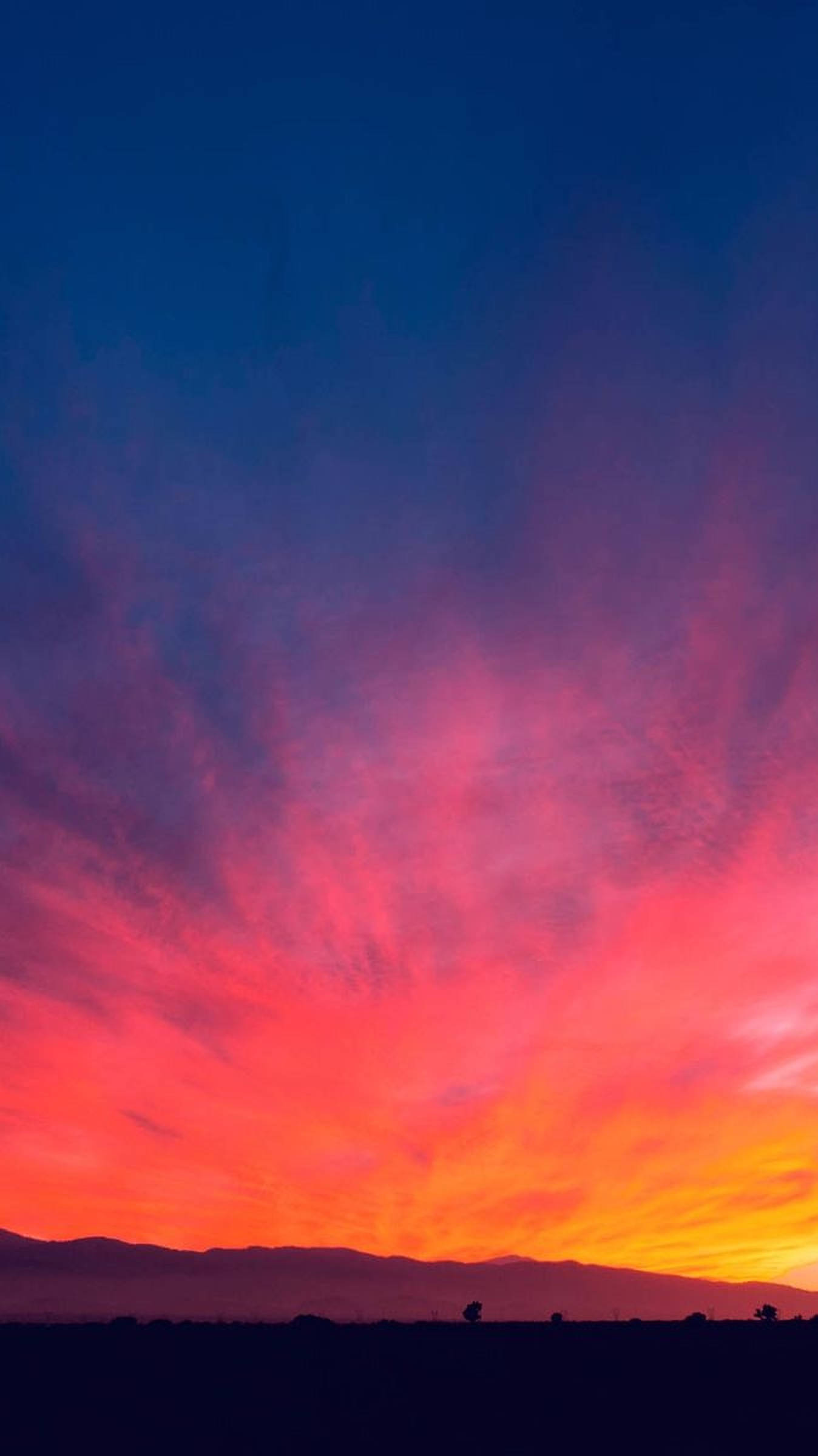 夕陽天空 桌布 壁紙 — 戲劇性的日落用火紅、橙色和深紫色在黑暗的山脈剪影上繪畫天空。