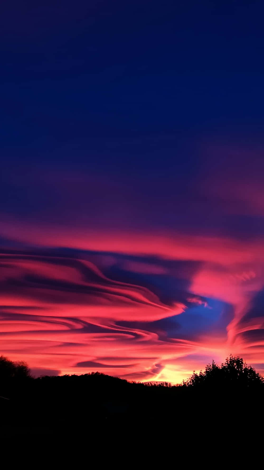 Clouds Aesthetics 桌布 壁紙 — 戲劇性的日落用火紅和深紫色的波浪在黑暗的樹線上描繪天空。