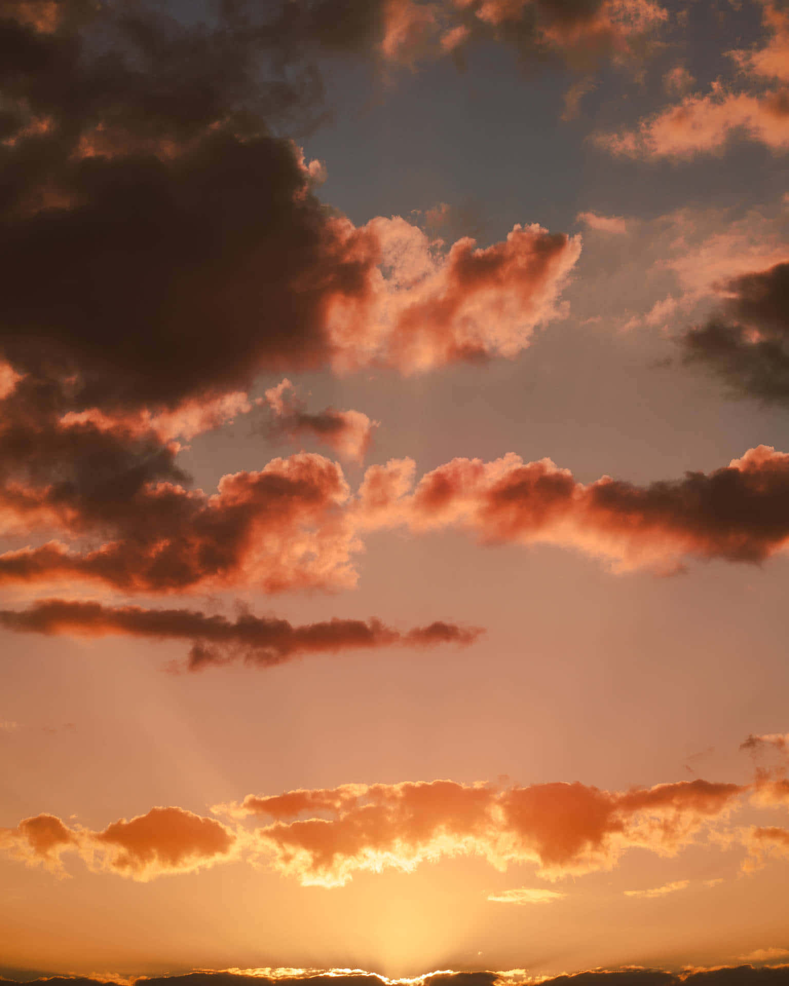 Clouds Aesthetics 桌布 壁紙 — 戲劇性的日落雲彩在漸深的藍天中發出火熱的橙色和粉紅色光芒，陽光穿透雲層。