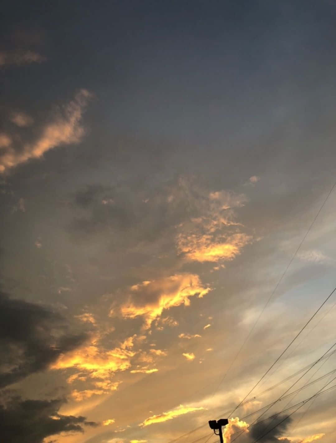 Aesthetic Sky 桌布 壁紙 — 戲劇性的日落雲彩在電線和電線桿剪影框住的昏暗天空中閃耀著金色光芒。