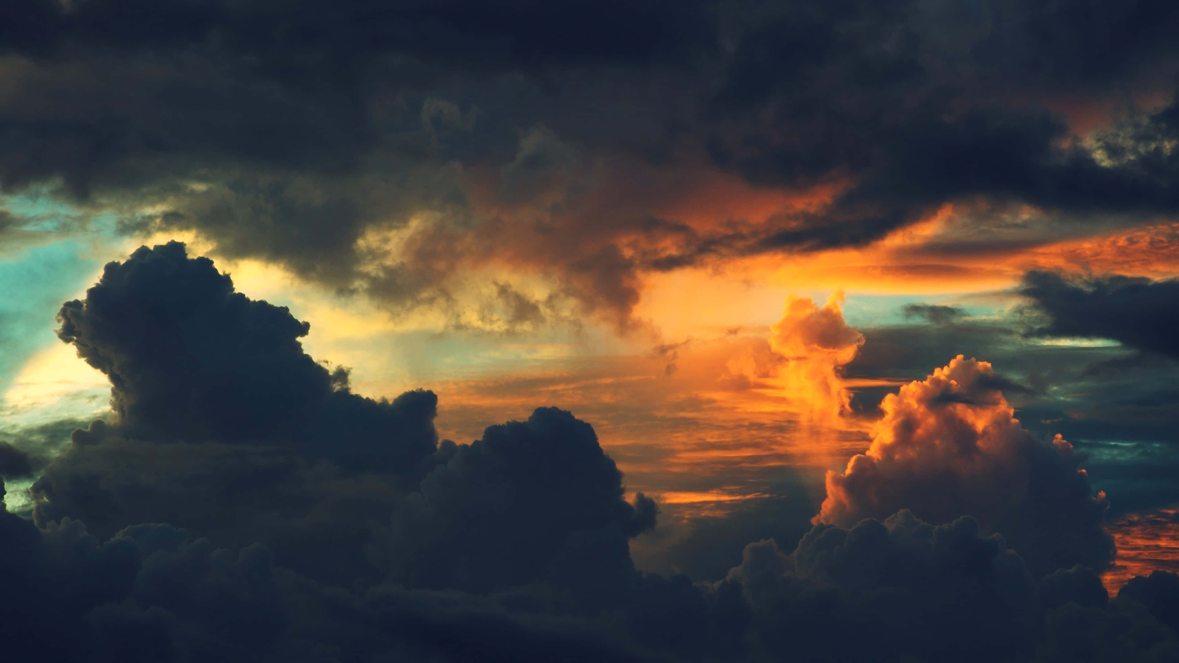 Clouds Aesthetics 桌布 壁紙 — 戲劇性的日落雲彩在黑暗暴風雨的天空中散發出火熱的橙色和金色光芒，陽光穿透雲層。