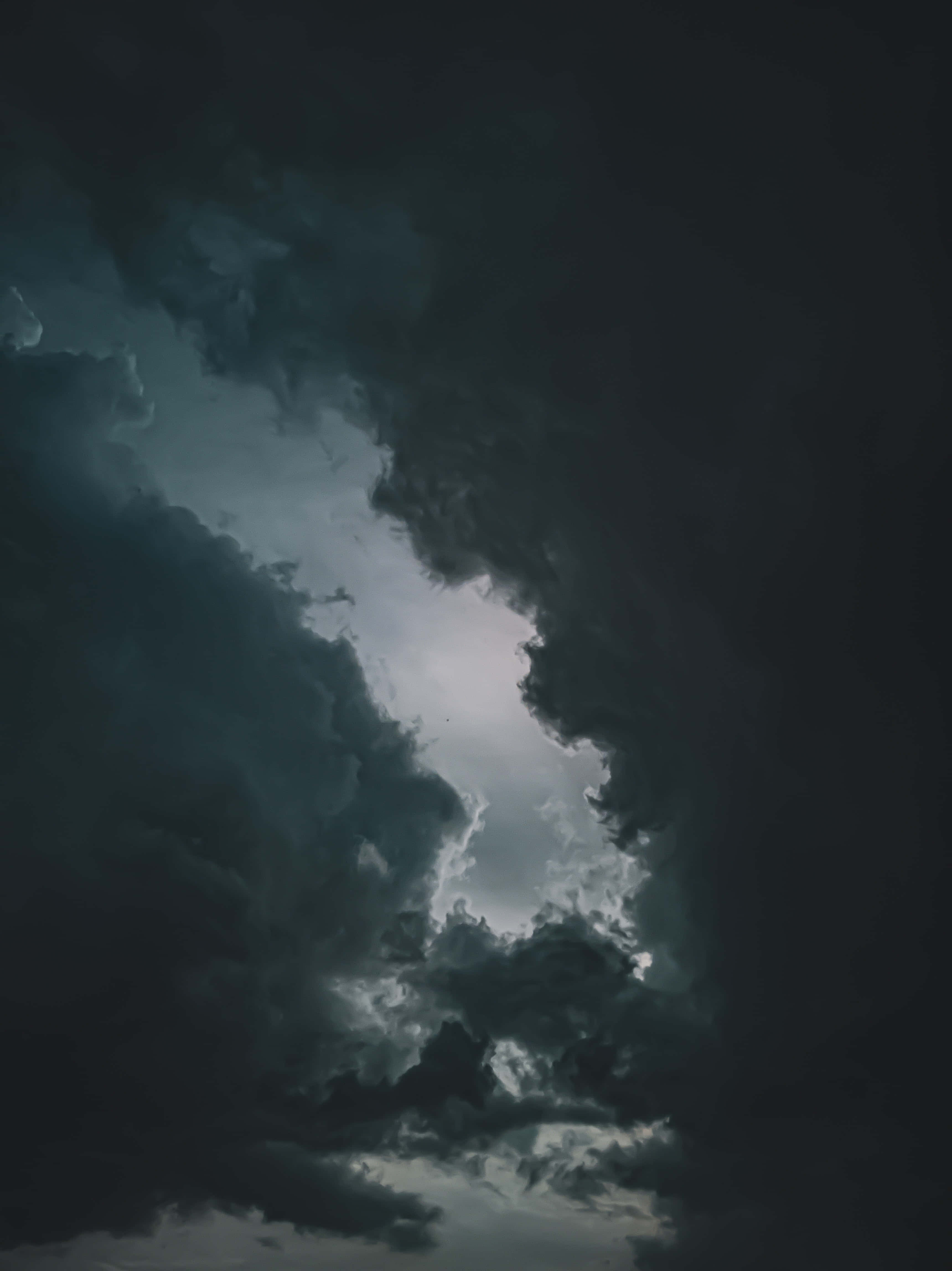 Cloudy Sky 桌布 壁紙 — 戲劇性的暗色暴風雲層分開，露出上方明亮發光的天空。