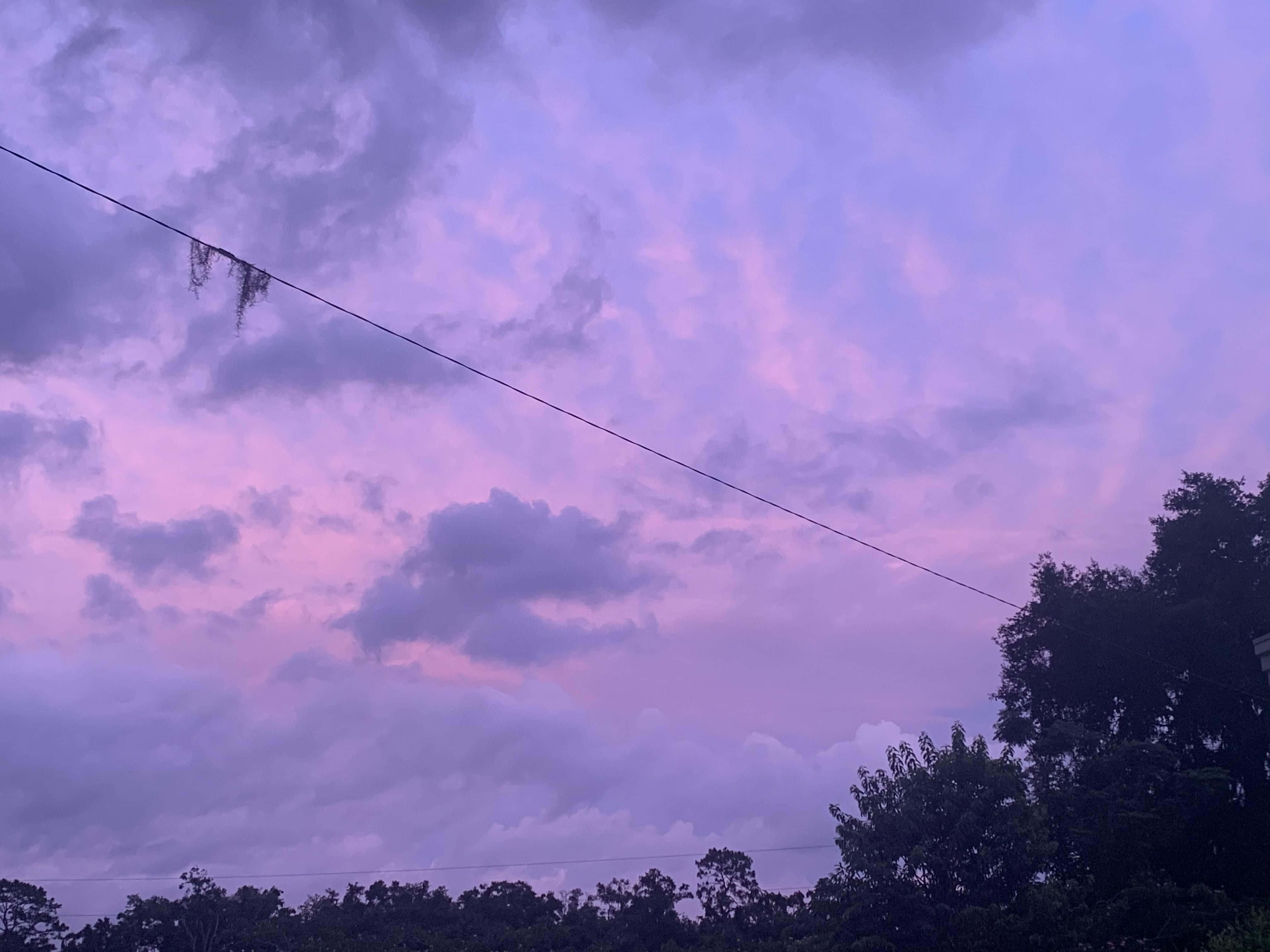 Aesthetic Cloud 桌布 壁紙 — 戲劇性的暮色天空，以柔和的紫色和粉紅色繪製，下方有深色雲朵和樹木剪影。