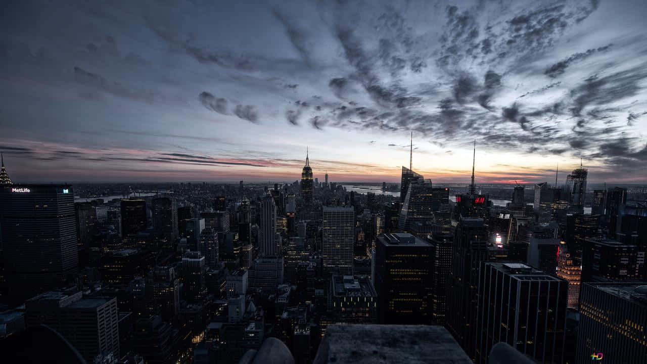 720p Ny City 桌布 壁紙 — 戲劇性的暮色天空帶有條紋雲彩，籠罩在廣闊的城市景觀之上，摩天大樓在漸暗的暮色中閃爍著溫暖的光芒。