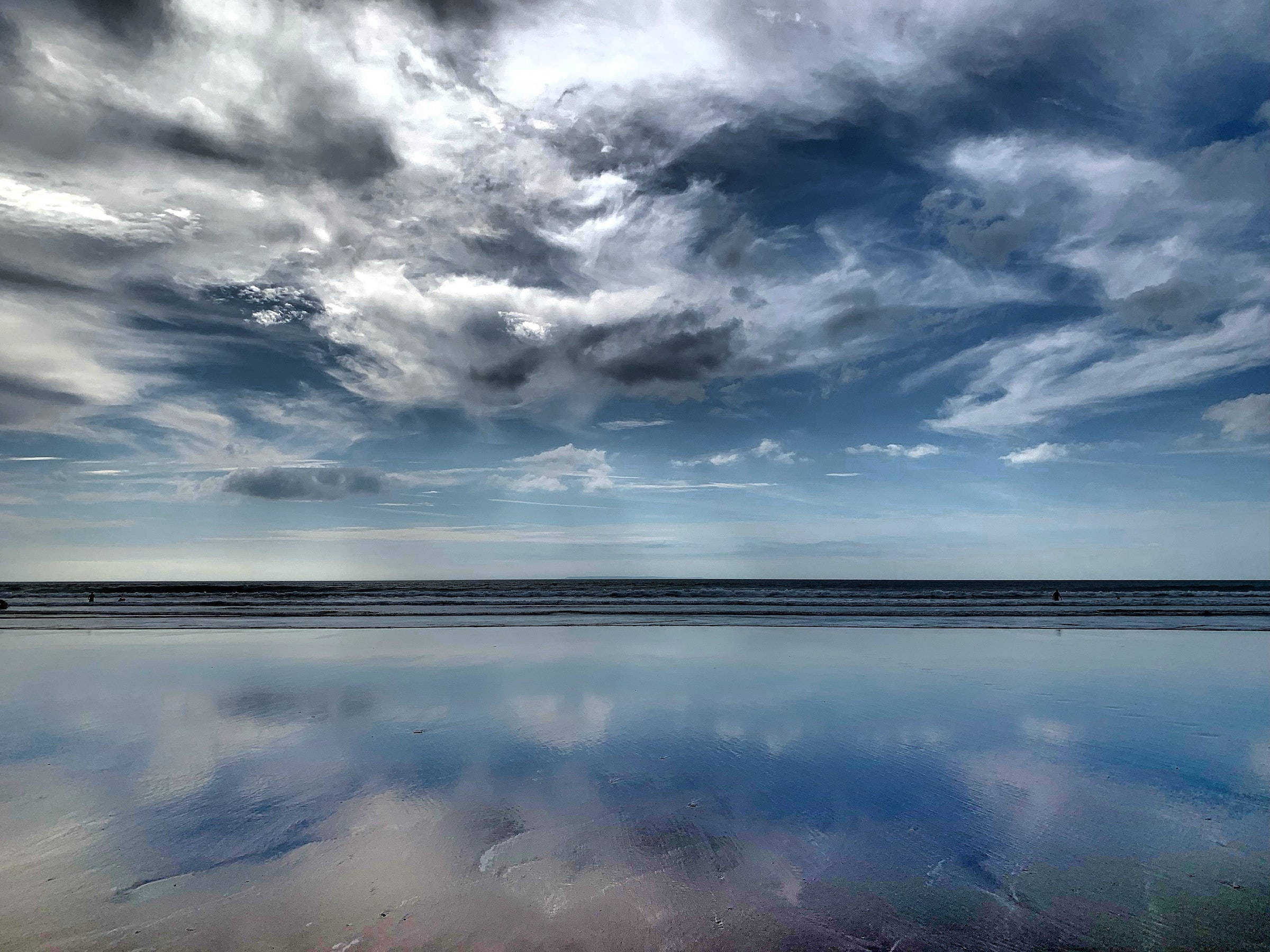海灘 桌布 壁紙 — 戲劇性的暴風雲在黃昏時分完美地倒映在平靜的海洋中，營造出寧靜而有力的海岸景象。