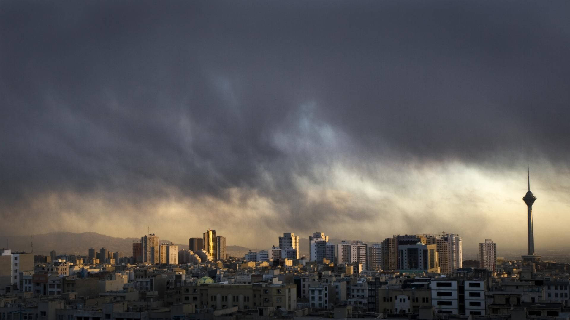 Tehran 桌布 壁紙 — 戲劇性的暴風雲籠罩德黑蘭的天際線，米拉德塔在黃昏時刺穿陰沉天空。
