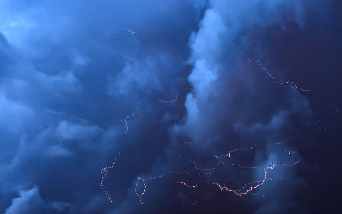 Thunderstorm 桌布 壁紙 — 戲劇性的暴風雲被鋸齒狀閃電照亮，劃過深藍色的天空。