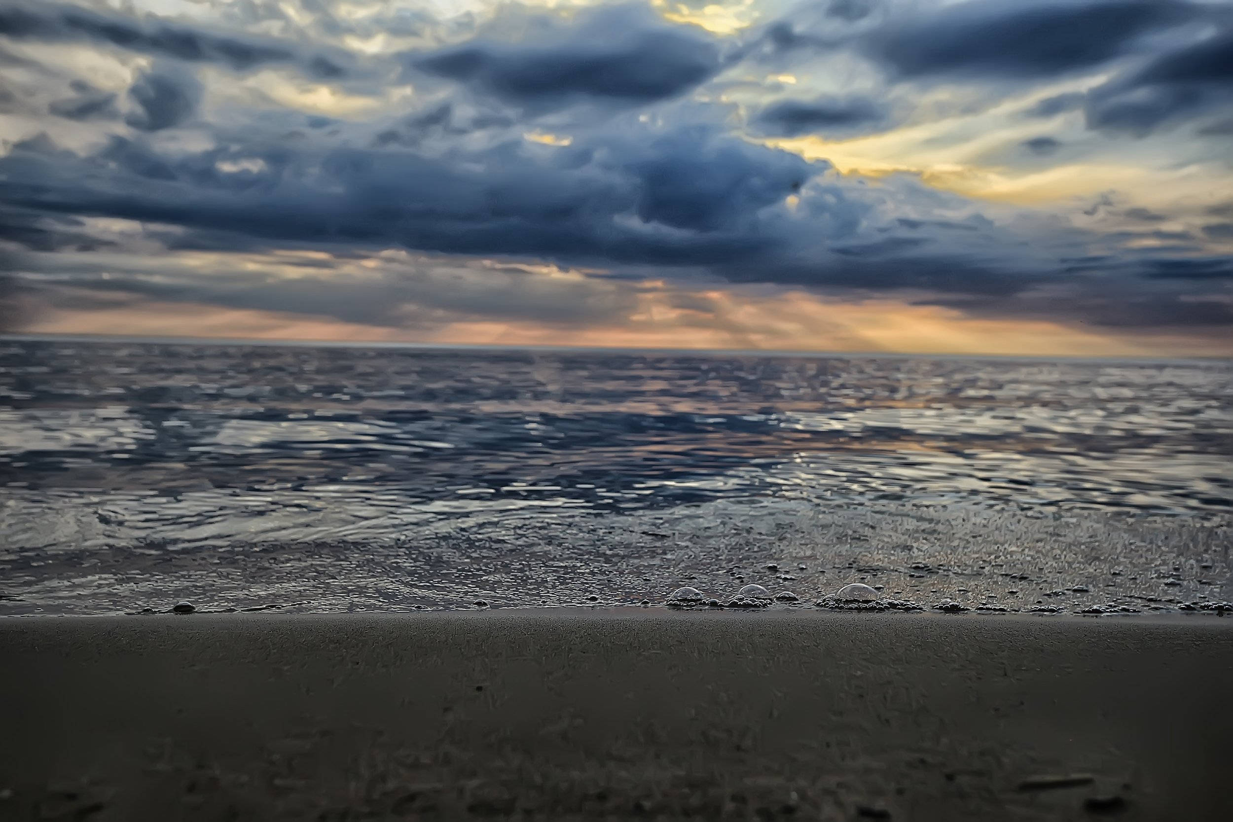 Beach Desktop 桌布 壁紙 — 戲劇性的暴風雲裂開，露出金色陽光，照耀著平靜的海洋與濕沙在黃昏時分相遇。