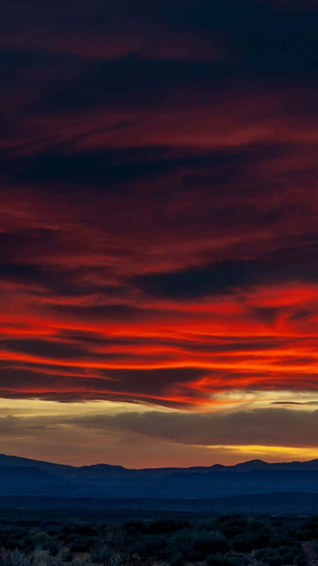 Clouds Aesthetics 桌布 壁紙 — 戲劇性的沙漠日落，在輪廓分明的山脈上空，將天空染成火紅和深紫色。