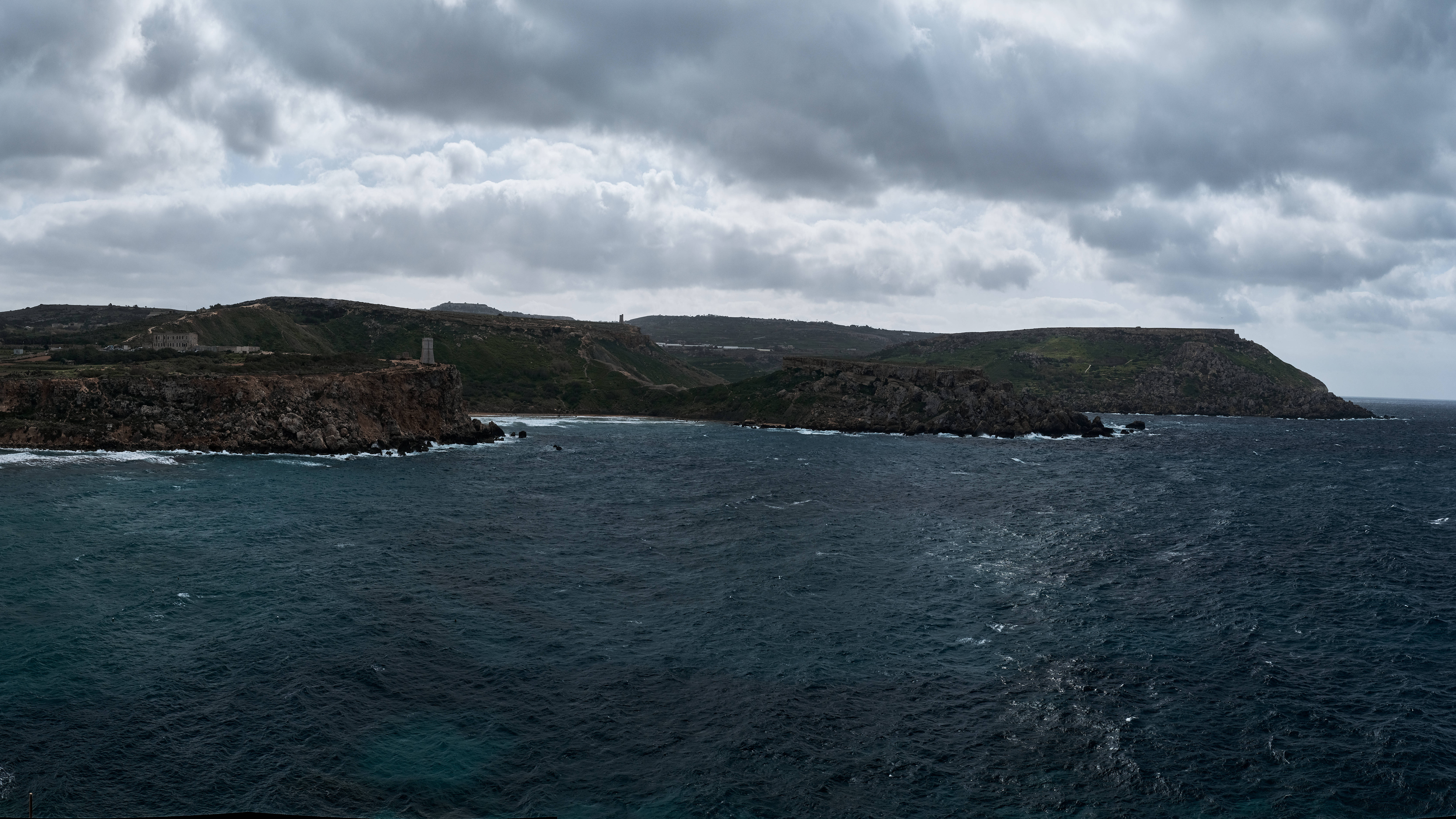 Malta 桌布 壁紙 — 戲劇性的海岸場景，黑暗的暴風雲籠罩著崎嶇的懸崖和翻騰的深藍色海浪。