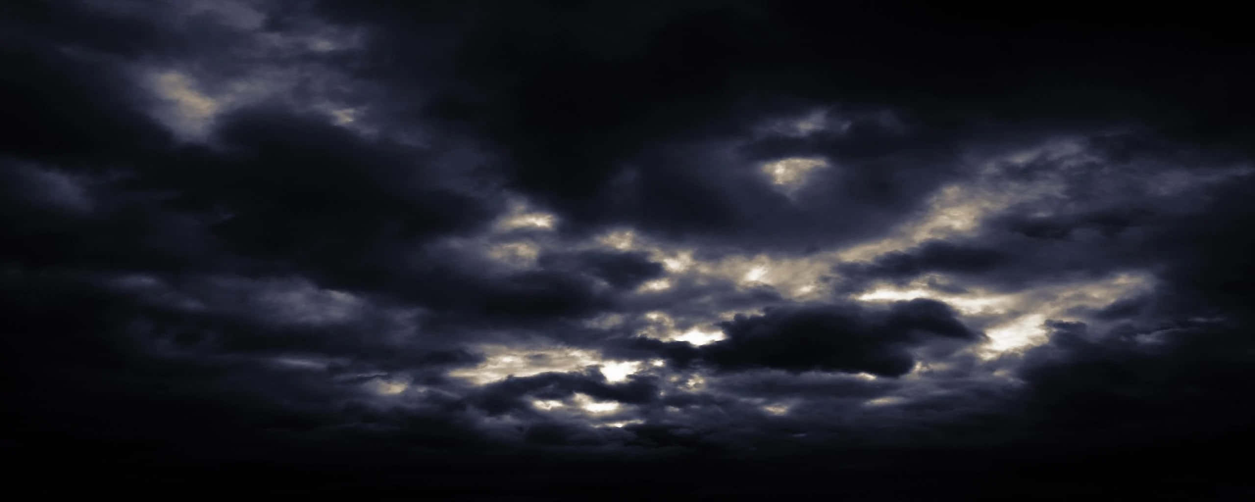Dark Sky 桌布 壁紙 — 戲劇性的烏雲在黑色天空中旋轉，邊緣閃耀著金色光芒。