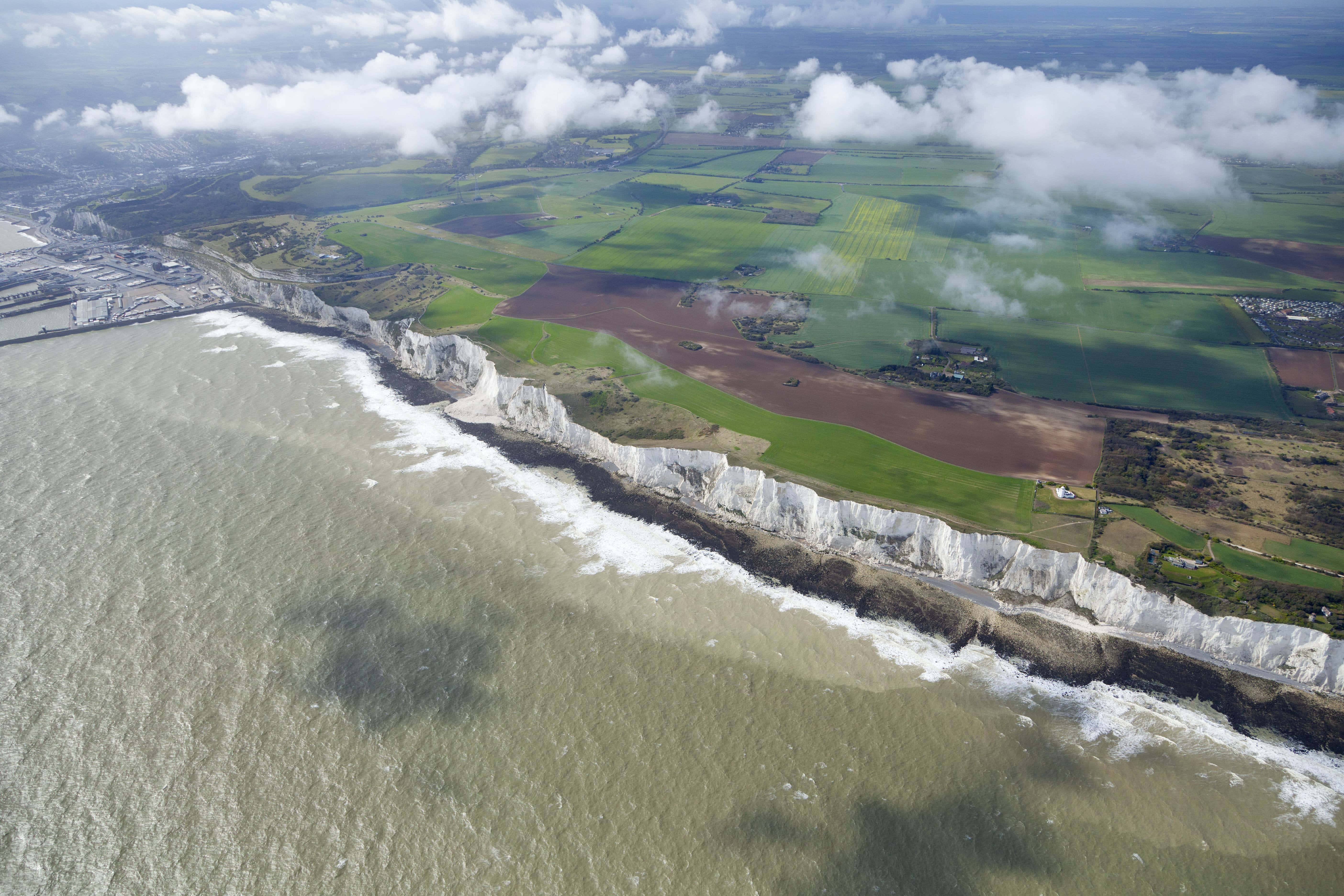 England 桌布 壁紙 — 戲劇性的白色白堊懸崖與洶湧的灰色海洋交匯的鳥瞰圖，上方有拼布般的綠色田野和散落的雲朵。