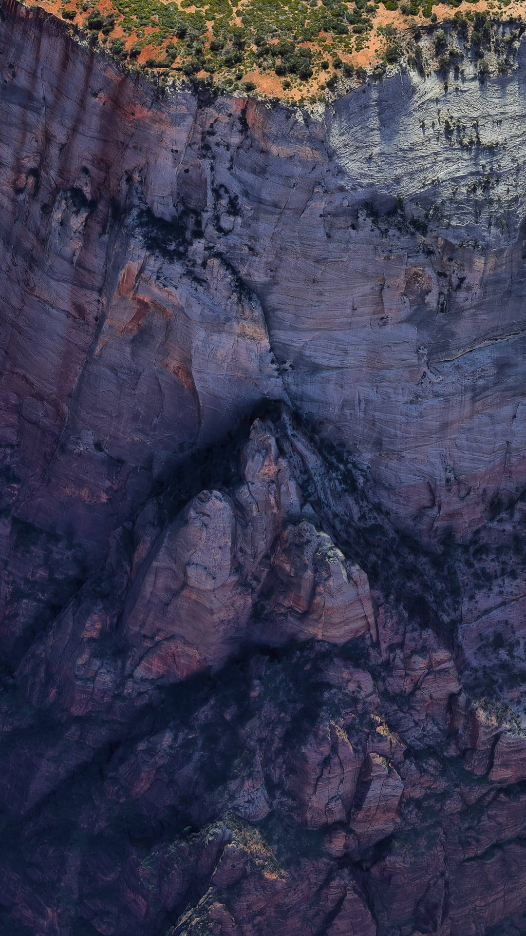 Rock 桌布 壁紙 — 戲劇性的空拍視角，展現層層疊疊的紅色岩石峽谷壁，稀疏的綠色植物攀附在懸崖邊緣。
