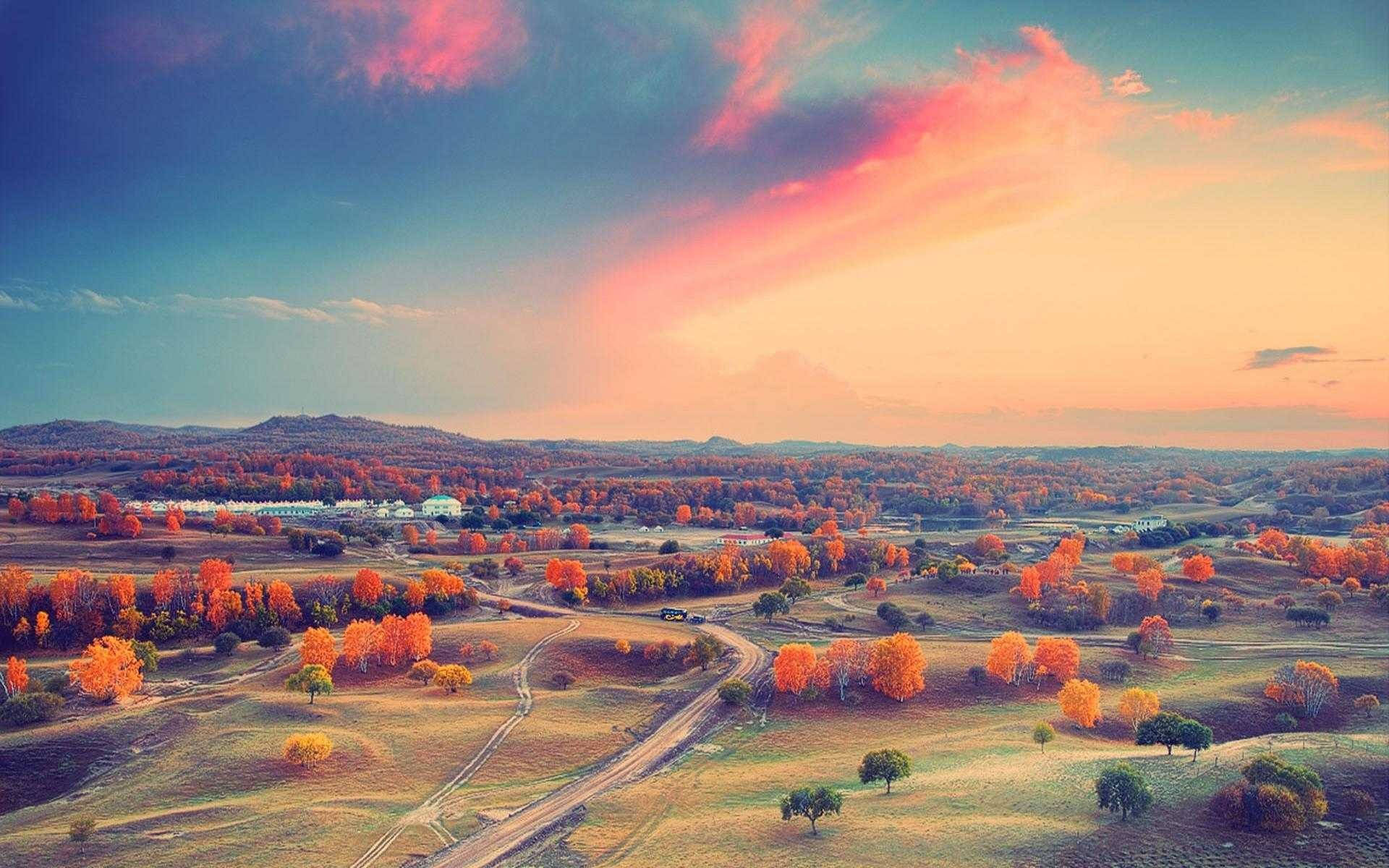 Horizon 桌布 壁紙 — 戲劇性的粉紅和藍色日落天空下，覆蓋著火熱橙色秋樹的起伏山丘的鳥瞰圖。