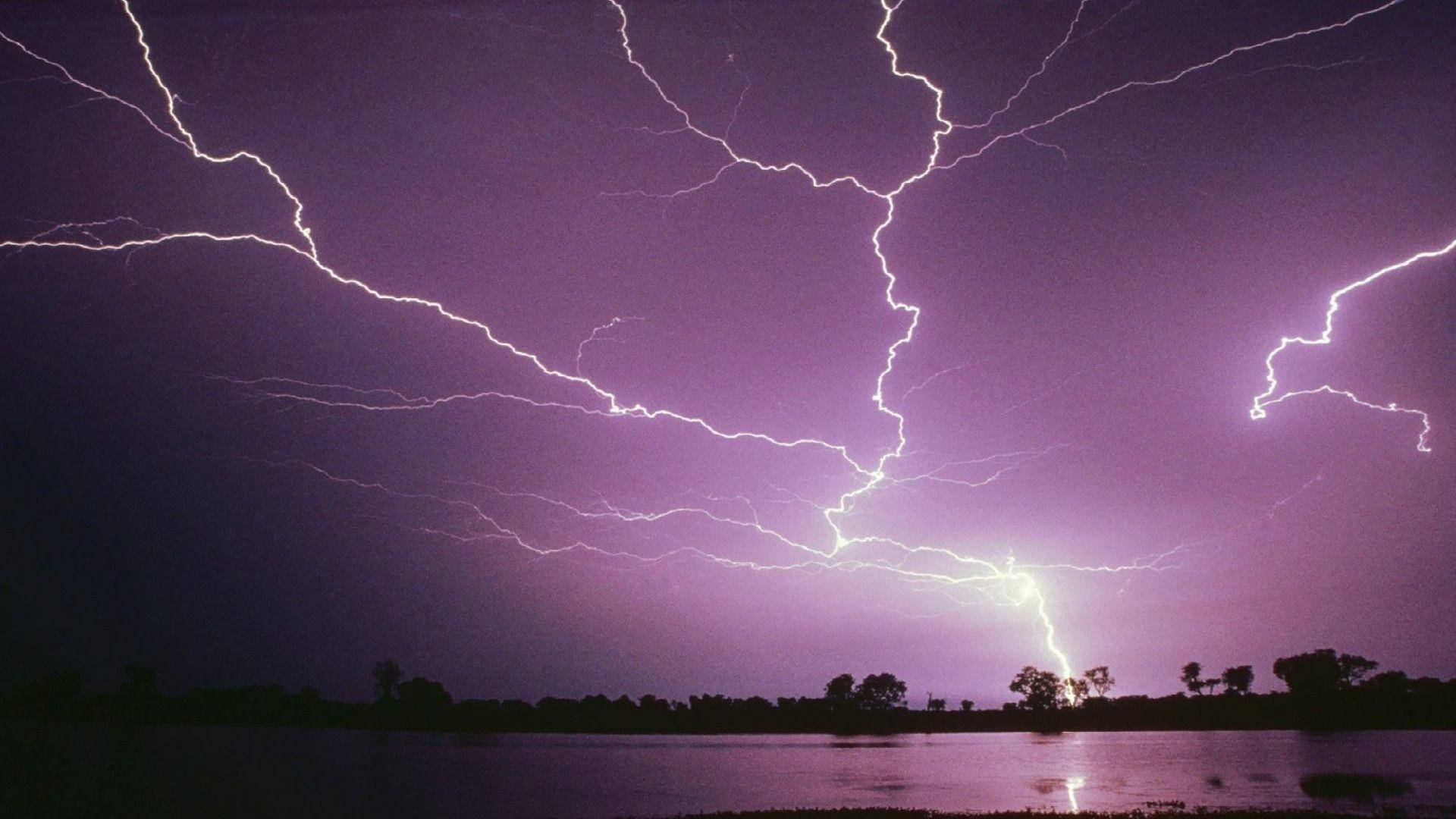 閃電 桌布 壁紙 — 戲劇性的紫色天空在平靜的湖面上閃爍著生動的白色閃電，湖面反射出暴風雨的電光。