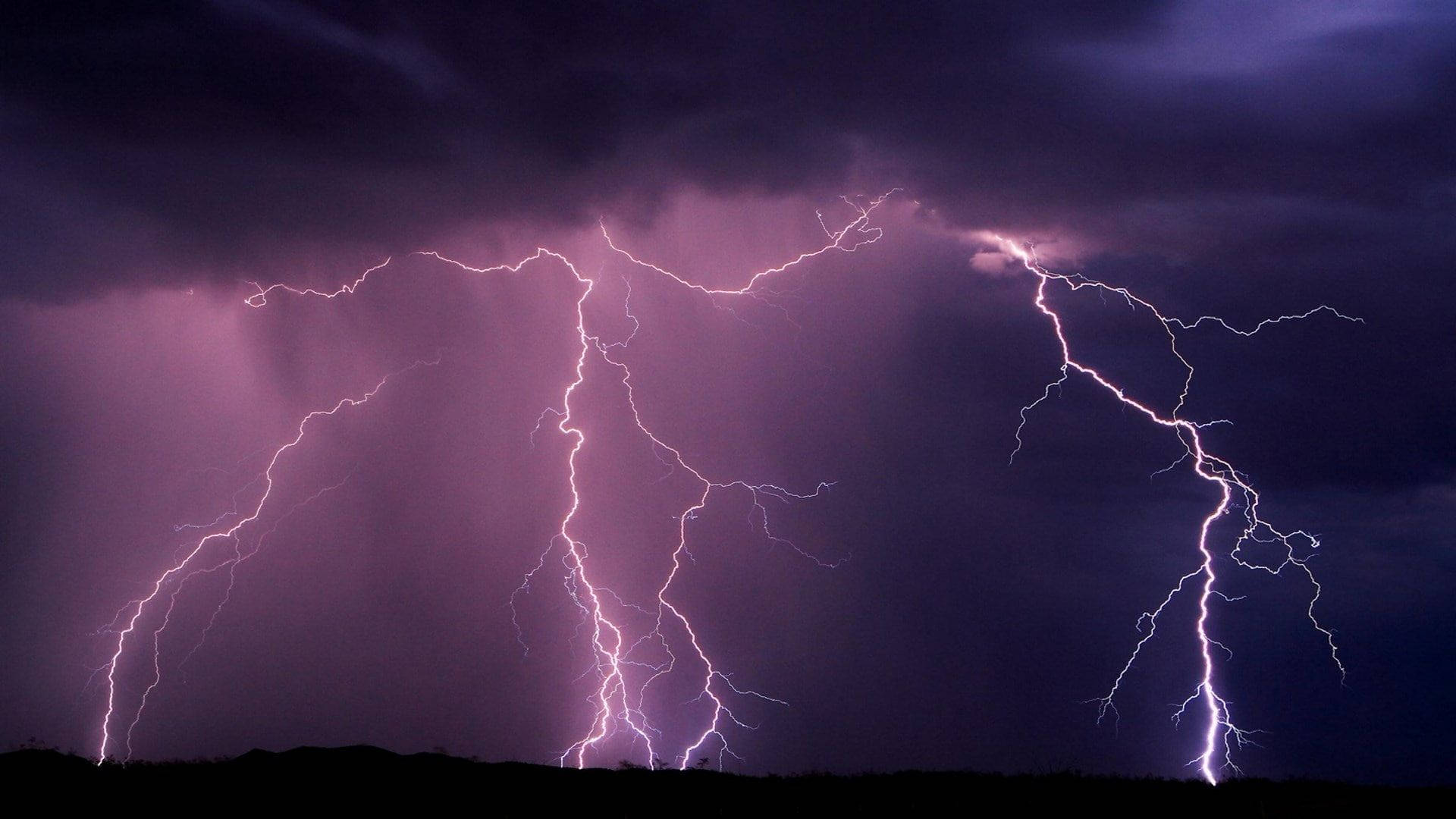 Aesthetic Lightning 桌布 壁紙 — 戲劇性的紫色閃電風暴照亮了剪影地平線上的黑暗天空。