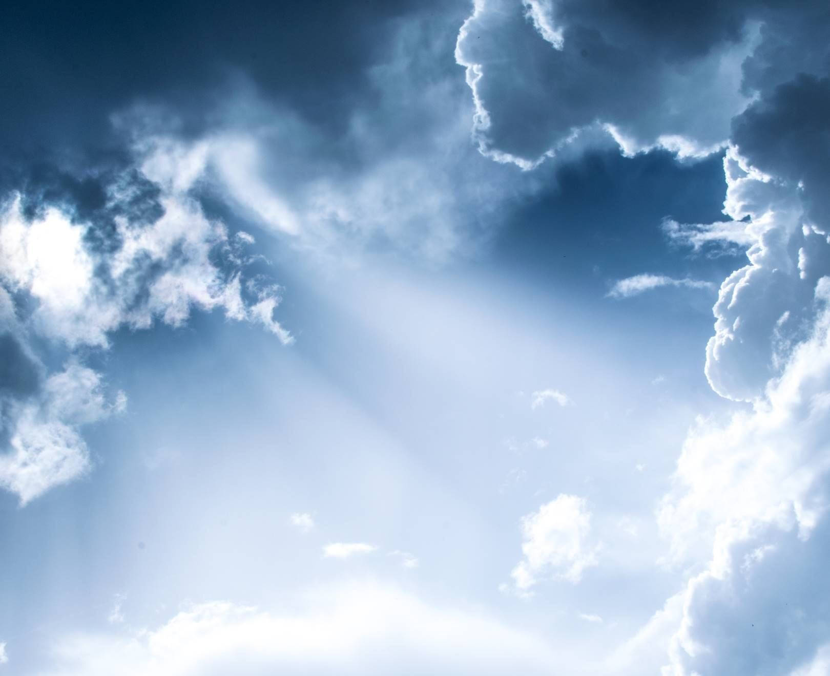 Heavenly Clouds 桌布 壁紙 — 戲劇性的藍天，陽光穿透蓬鬆的白雲，營造出寧靜而空靈的氛圍。