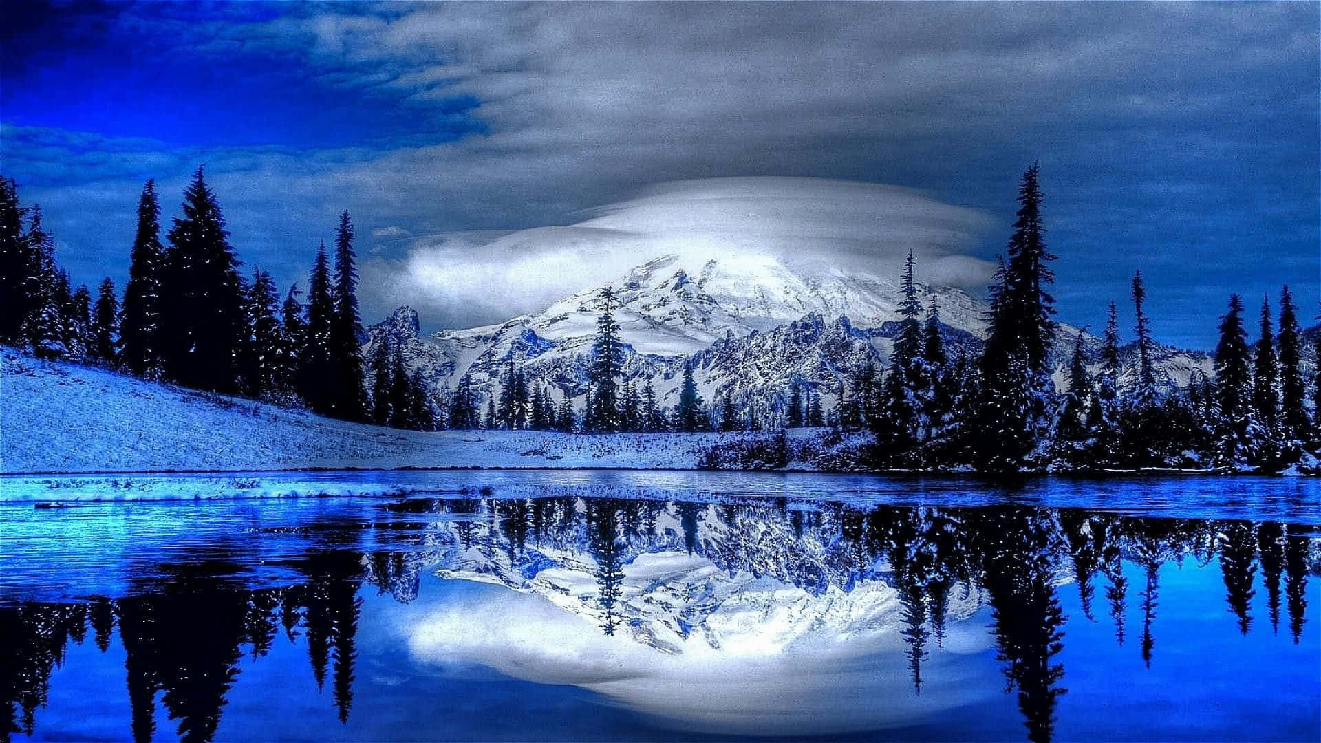 冬季桌面 桌布 壁紙 — 戲劇性的藍天下，白雪覆蓋的山峰完美地倒映在平靜的冰湖中，四周環繞著常青樹。