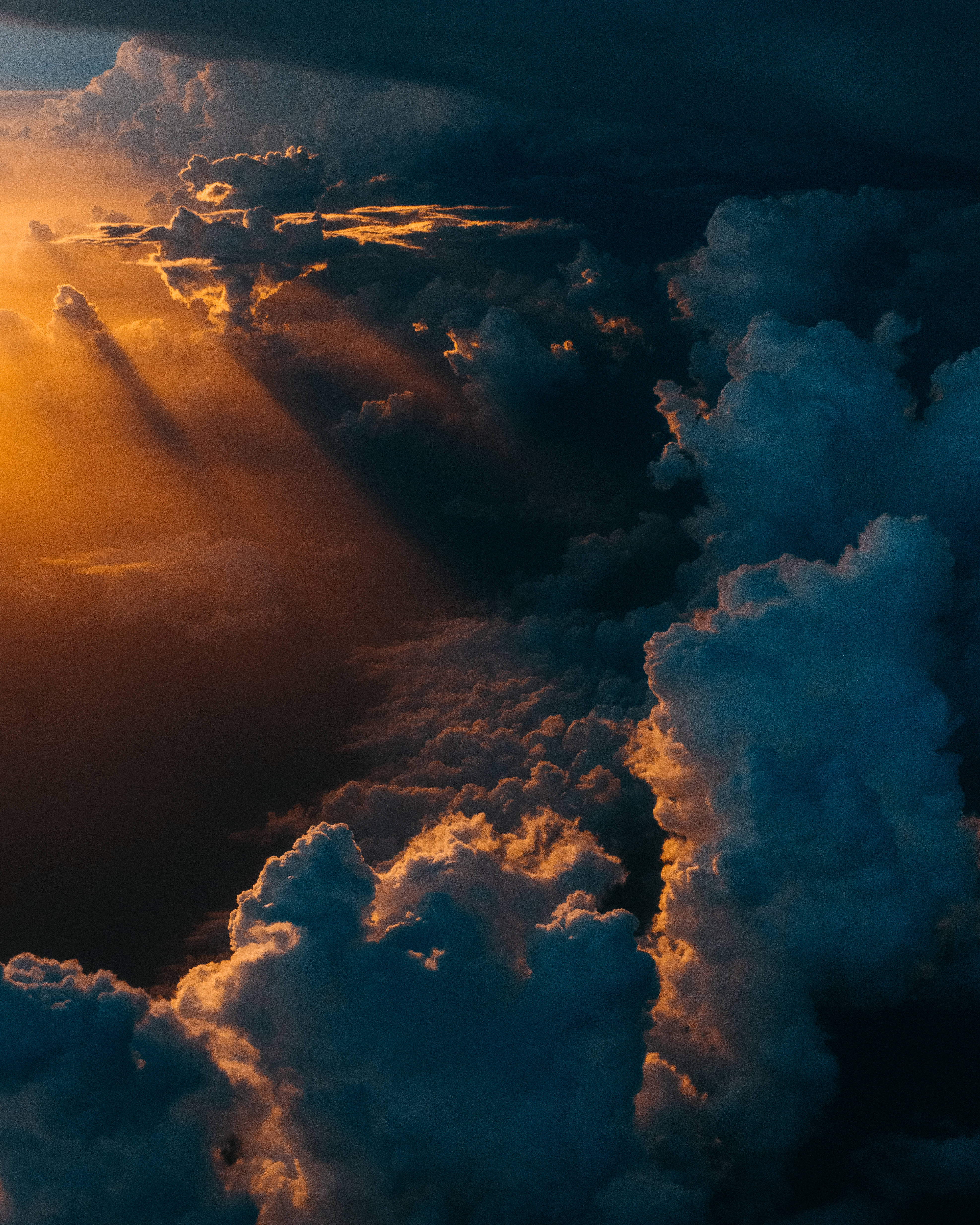 太空 桌布 壁紙 — 戲劇性的金色陽光穿透高聳的雲層，在廣闊的藍色和橙色天空中投射出空靈的光芒。