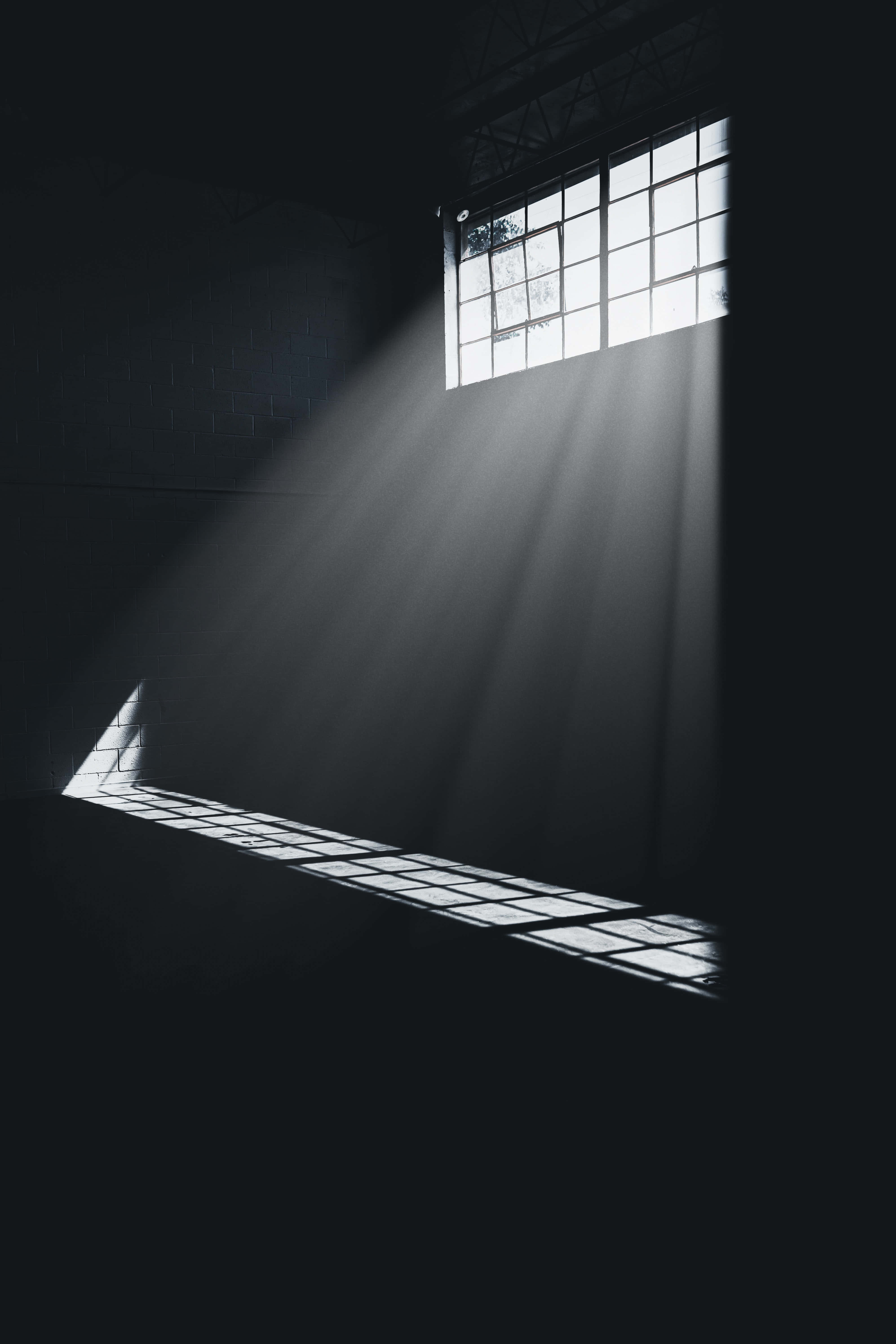 Dark Room 桌布 壁紙 — 戲劇性的陽光穿過高窗，在黑暗空曠的工業房間中投下銳利的陰影。