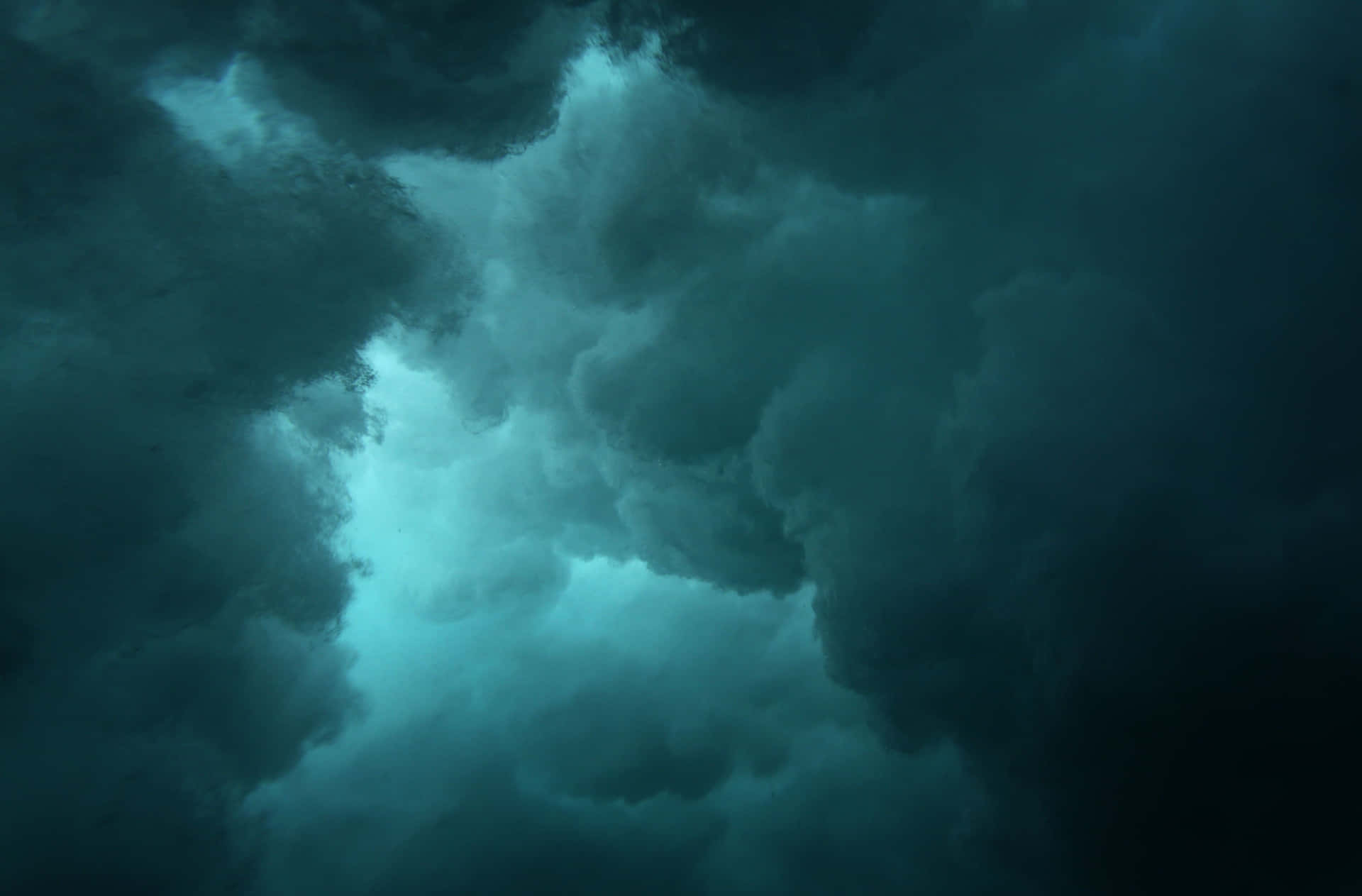 Cyan Aesthetic 桌布 壁紙 — 戲劇性的青色和黑色暴風雲旋轉，光線穿透陰沉的天空。