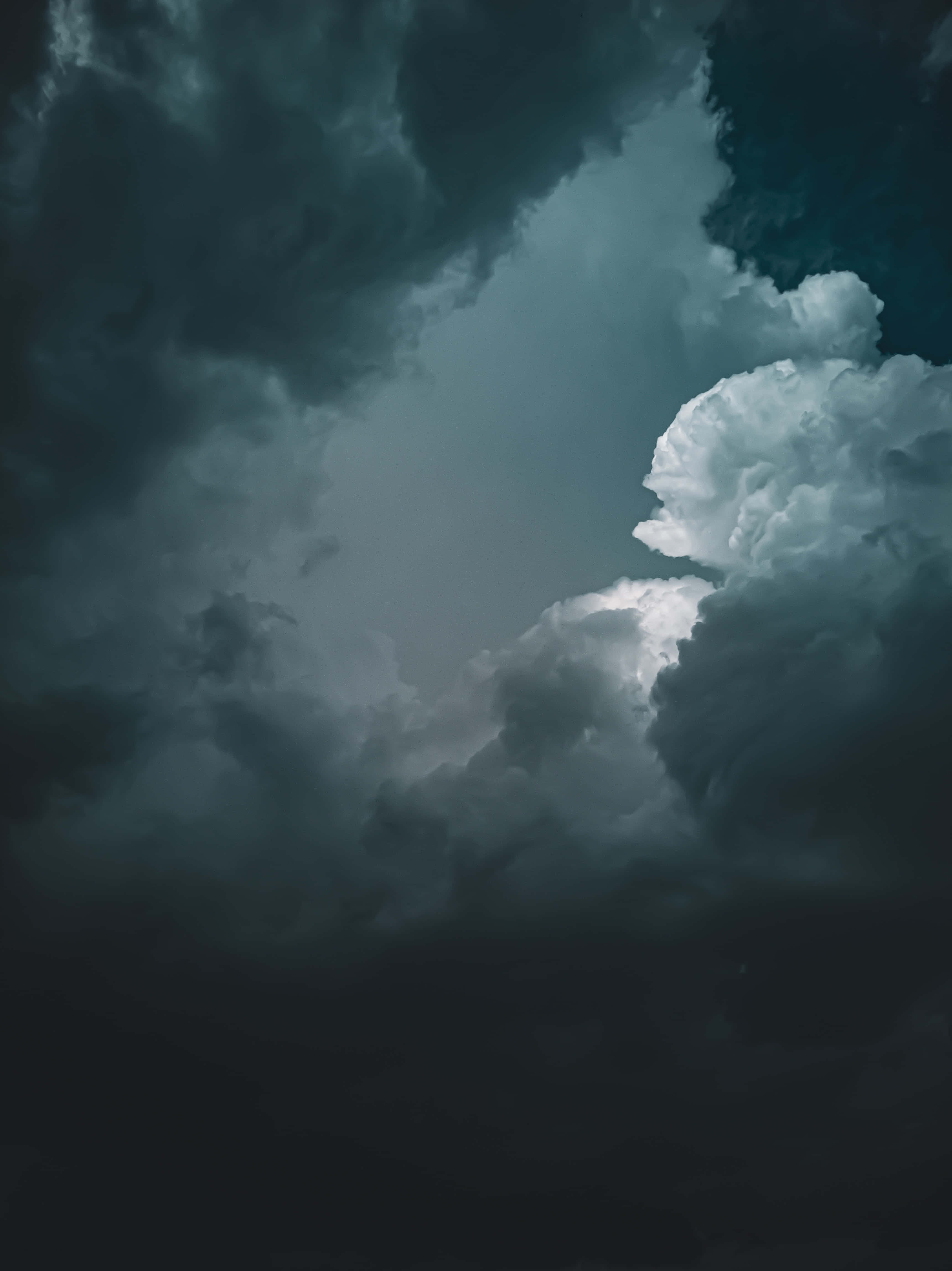 Dark Clouds 桌布 壁紙 — 戲劇性的風暴雲層以深藍綠色和炭灰色調旋轉，一縷明亮的雲層穿透陰霾。