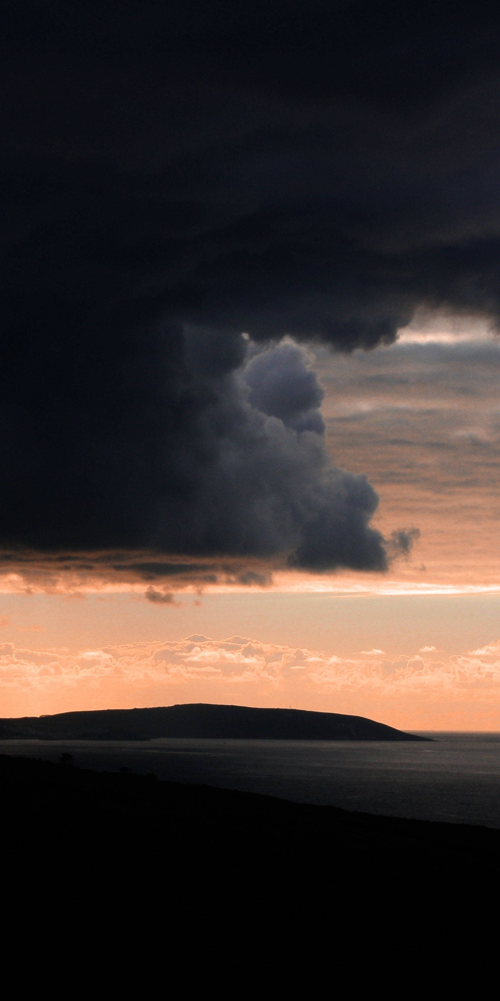 Clouds Aesthetics 桌布 壁紙 — 戲劇性的風暴雲籠罩著日落時分的剪影海岸線，在地平線上投射出熾熱的橙色光芒。