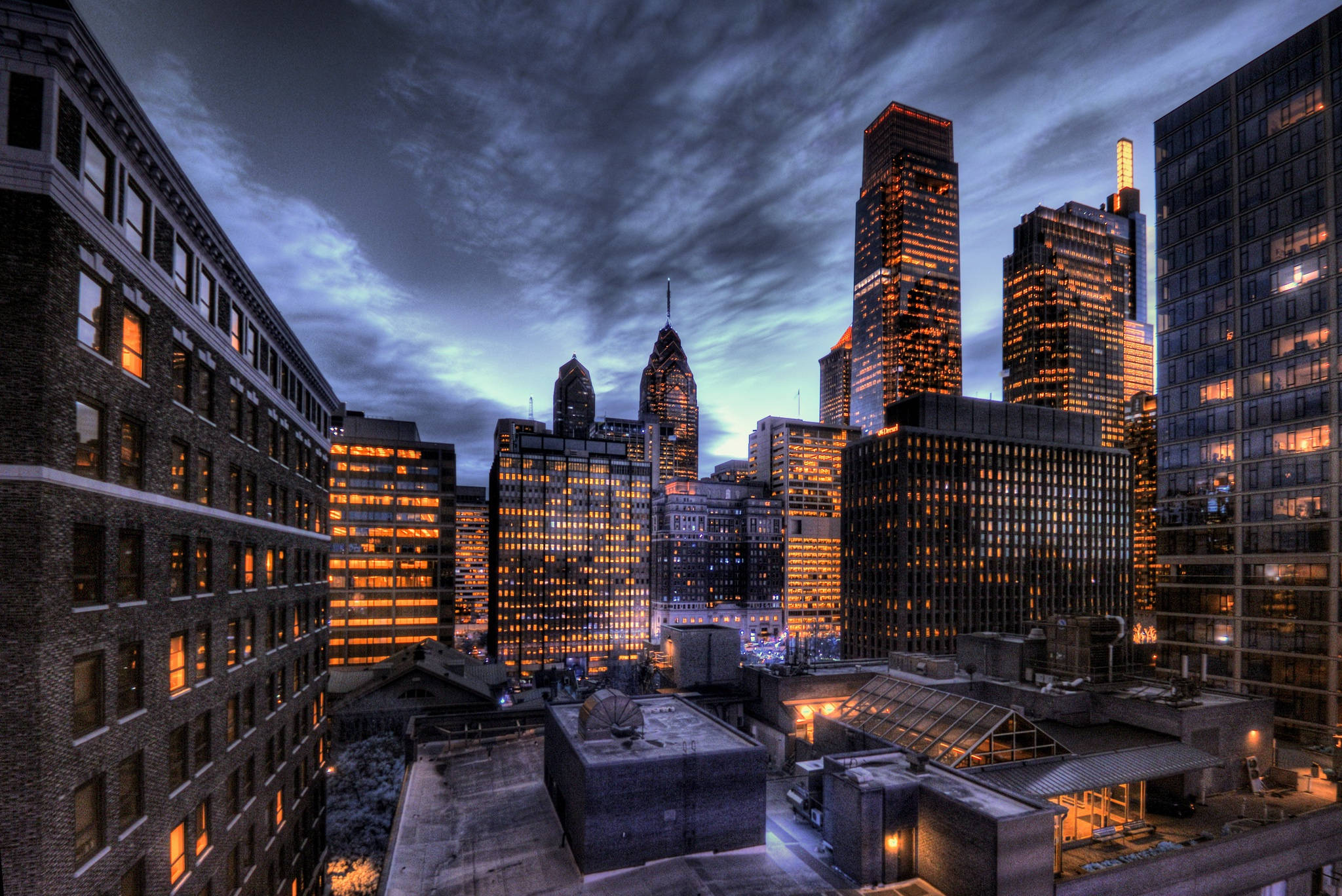Philadelphia 桌布 壁紙 — 戲劇性的黃昏城市景觀，高聳的摩天大樓在憂鬱的紫色和藍色天空下溫暖地發光。