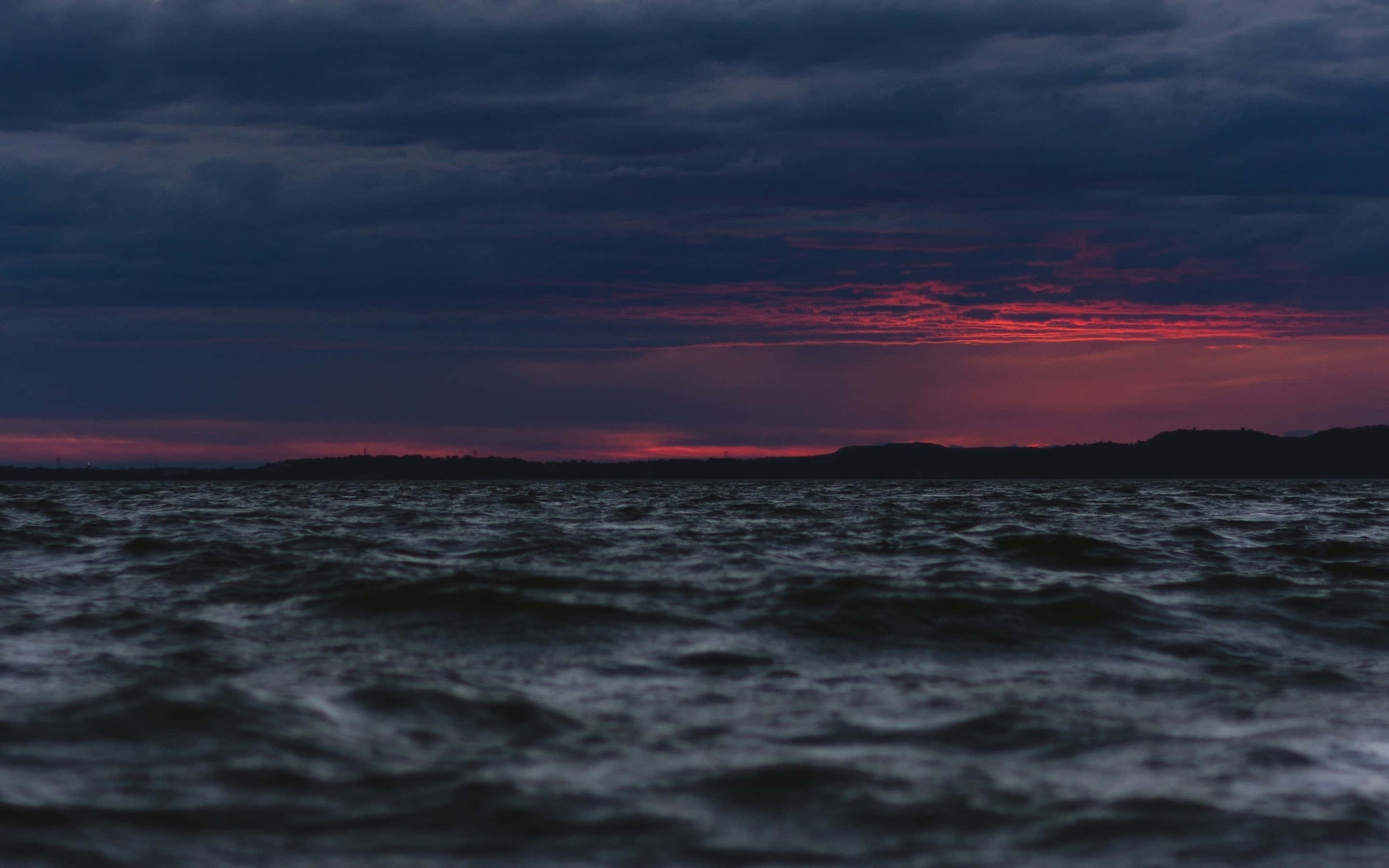 Black Sea 桌布 壁紙 — 戲劇性的黃昏天空，火紅的雲彩在黑暗洶湧的大海和遠處陸地輪廓之上。