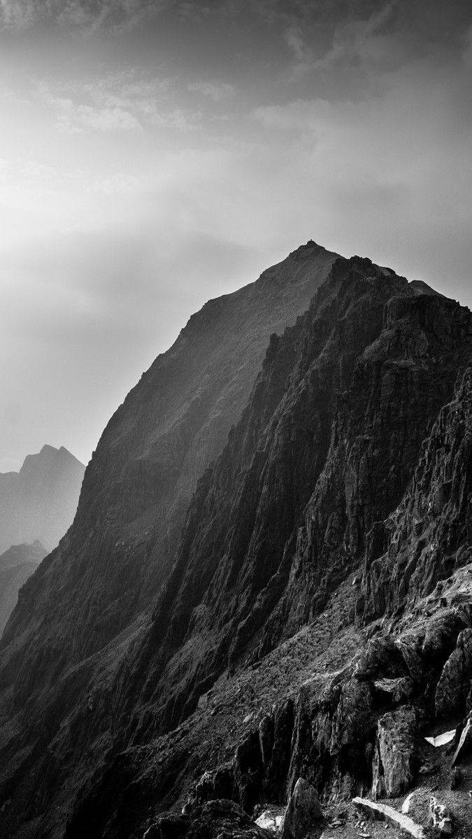 Black And White iPhone 桌布 壁紙 — 戲劇性的黑白山峰在陰雲密佈的天空下陡峭聳立，岩石表面紋理分明。