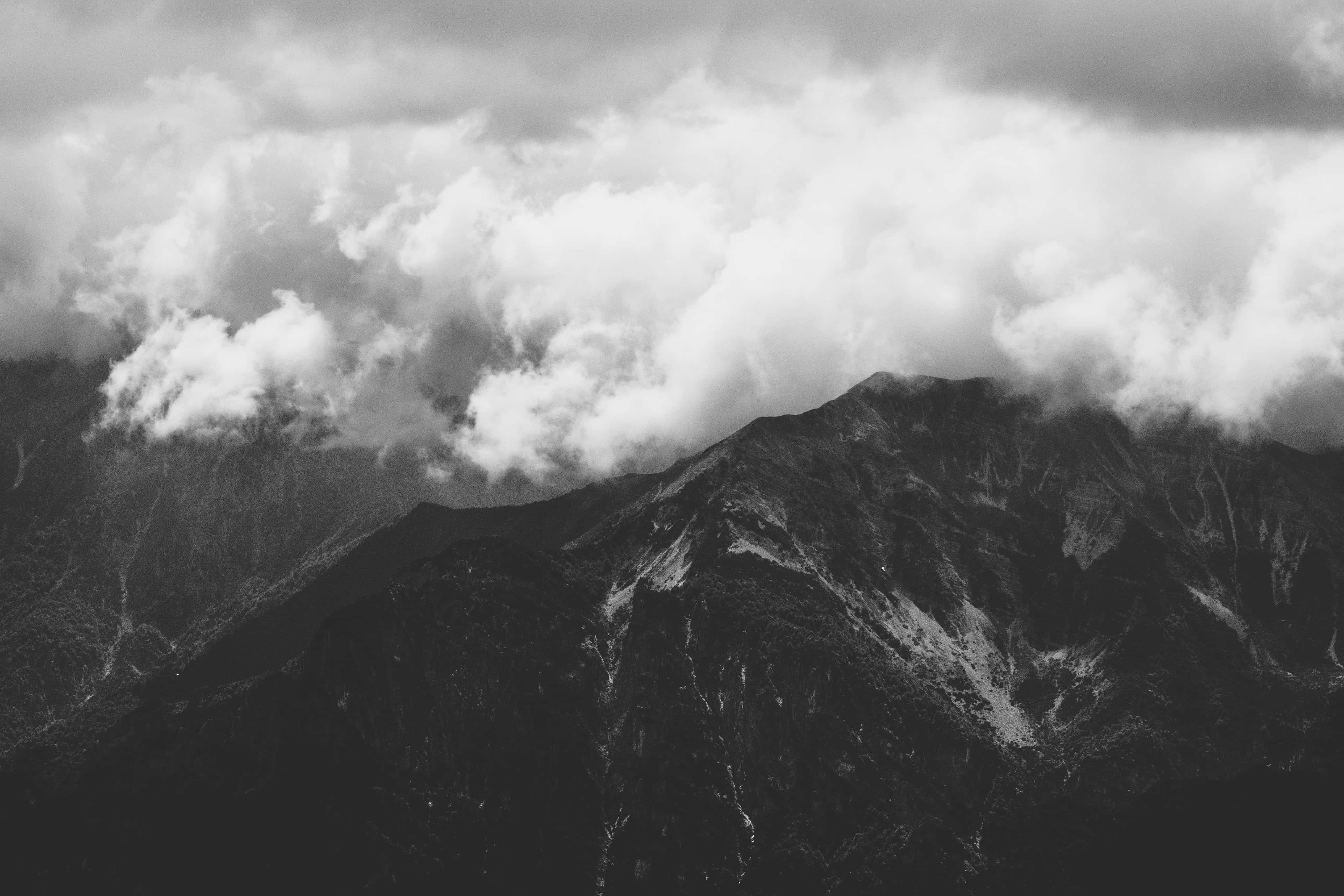 Dark Mountain 桌布 壁紙 — 戲劇性的黑白山峰穿透厚厚旋轉的雲層，在陰沉天空下。
